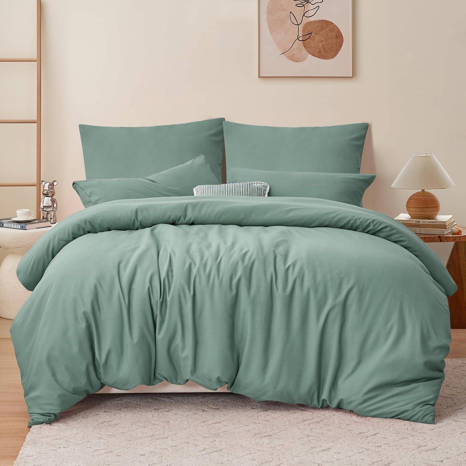 Ein ordentlich gemachtes Bett mit einer grünen Bettdecke, zwei Kissen und einem Zierkissen. Neben dem Bett stehen ein kleiner Nachttisch mit einer Lampe und ein Regal.