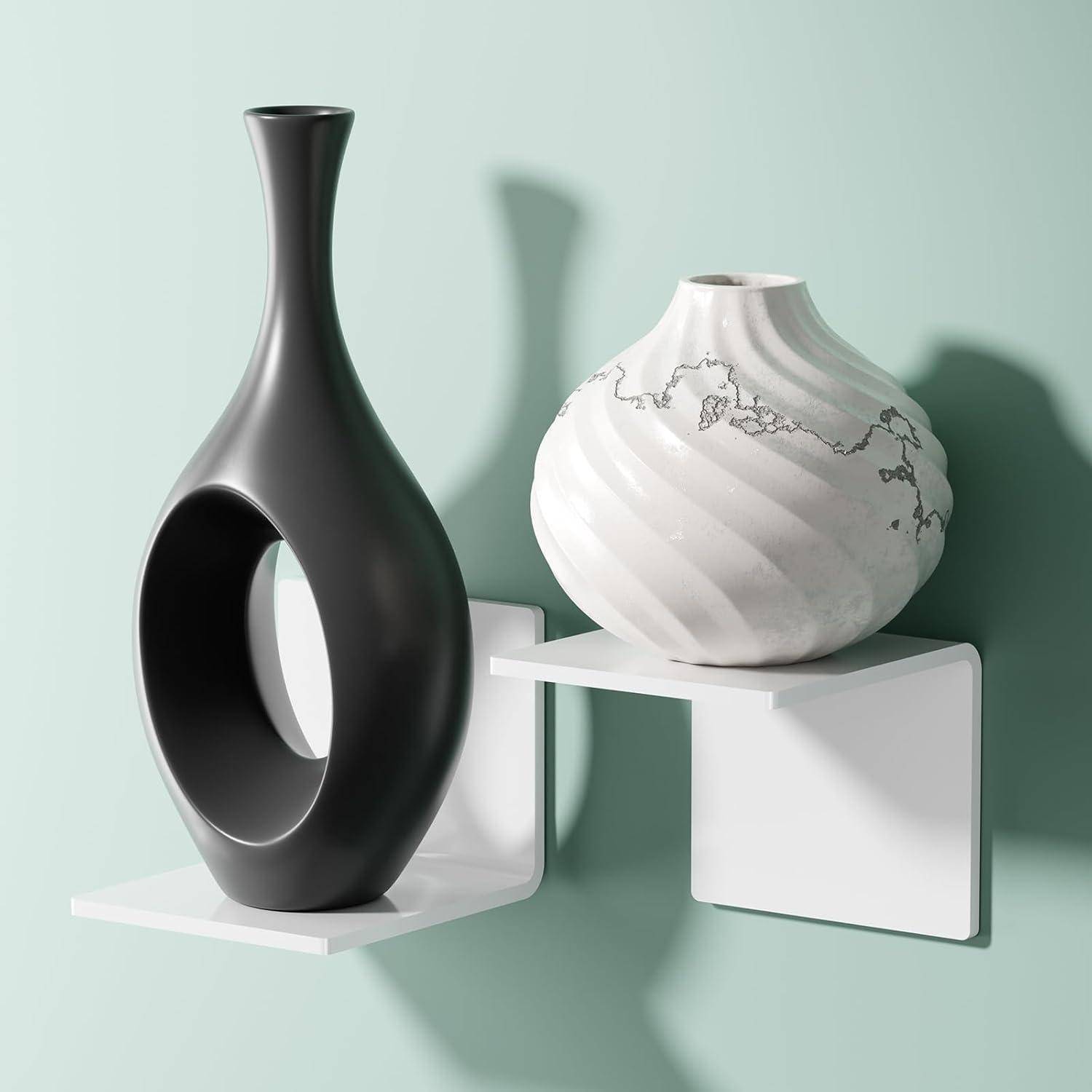 Eine minimalistische Szene mit zwei Vasen auf einem weißen Wandregal vor einer mintgrünen Wand. Eine Vase ist schwarz, hoch und hat eine offene Mitte; die andere ist weiß mit einem abstrakten Muster.