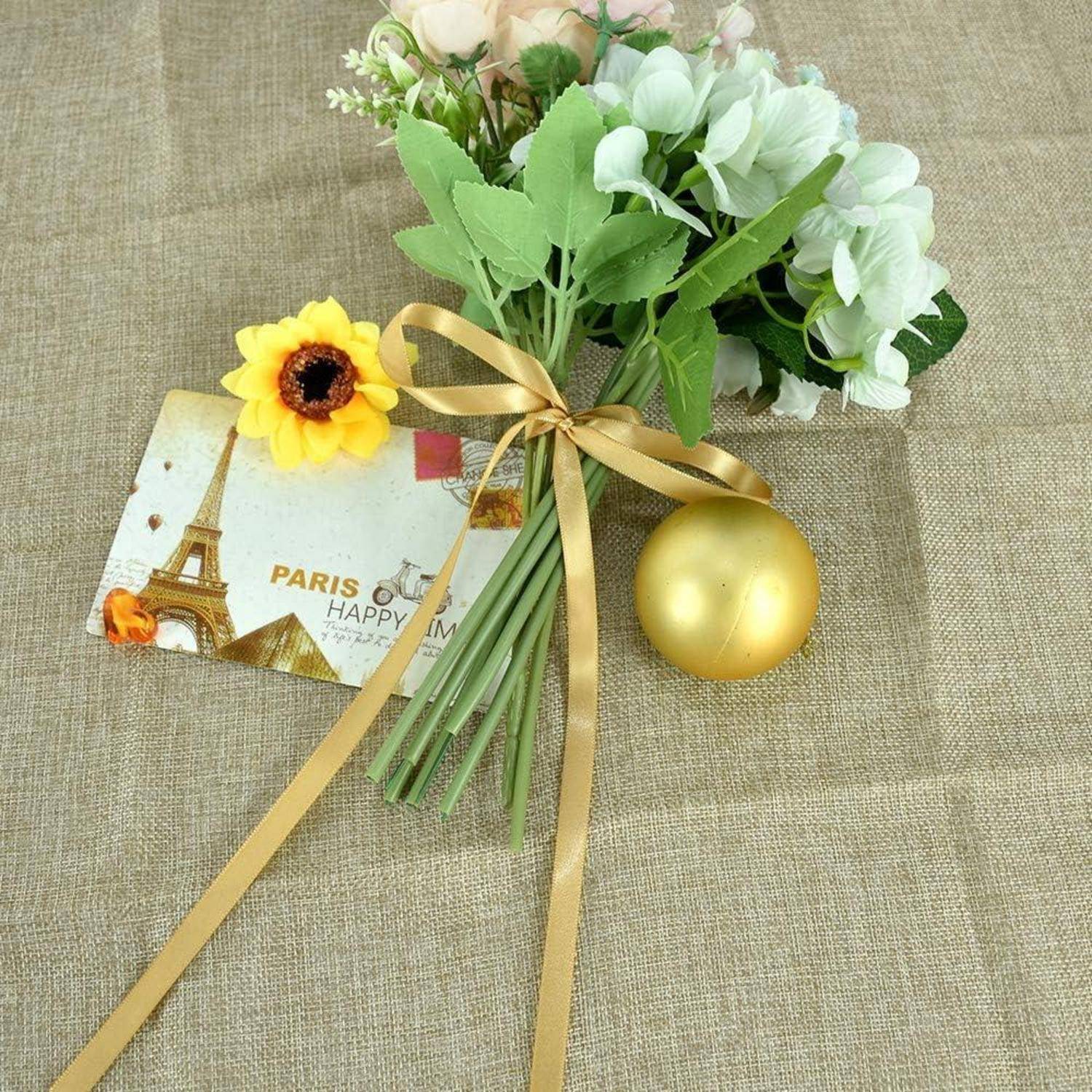 Ein kleiner Blumenstrauß aus weißen und gelben Blüten mit grünen Blättern, ein goldenes Band, eine goldene Verzierung und eine Postkarte mit dem Eiffelturm.