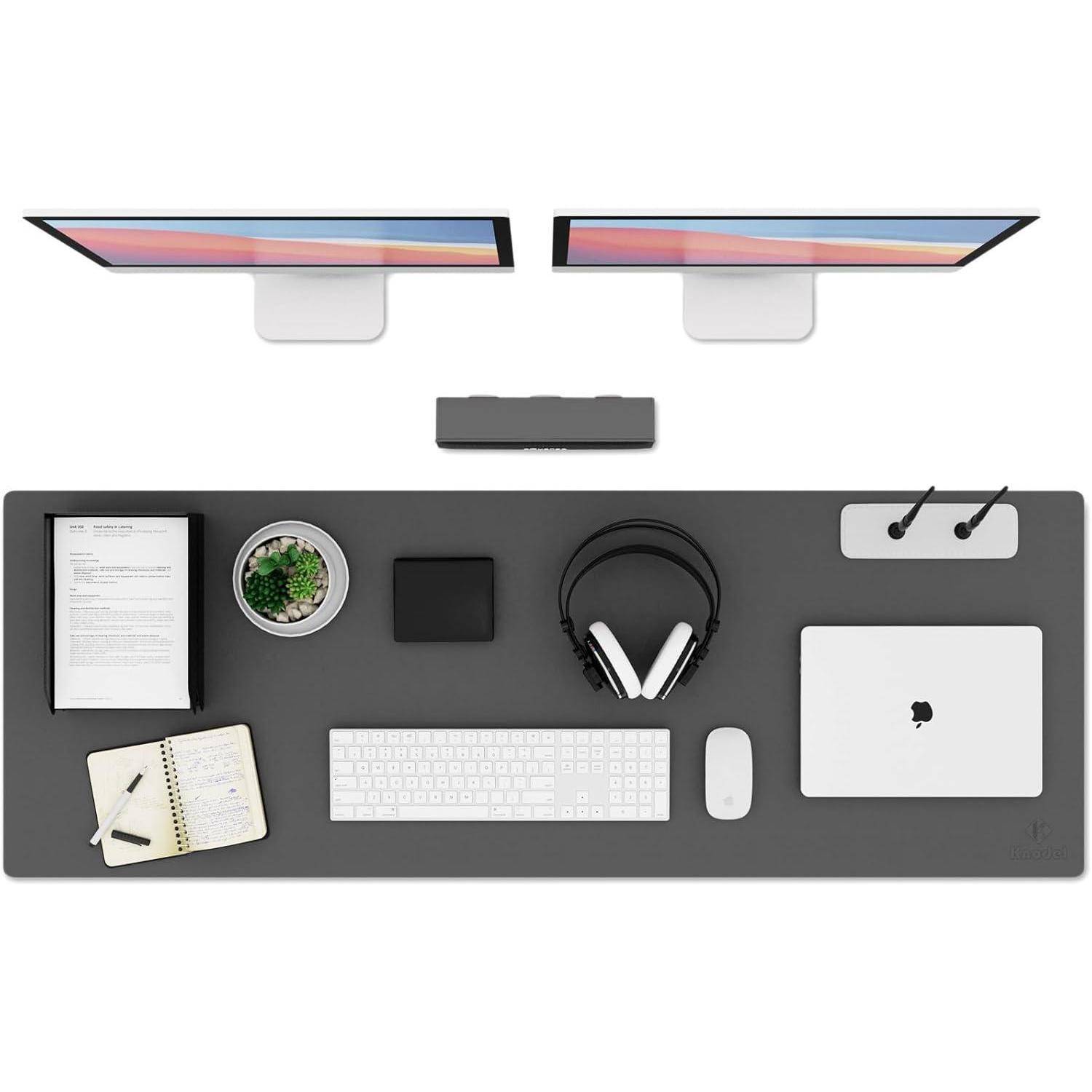 Ein aufgeräumter Schreibtisch mit zwei Monitoren, einer Tastatur, einer Maus, Kopfhörern, einem Laptop, Notizblöcken und einer kleinen Pflanze, die ordentlich angeordnet sind.