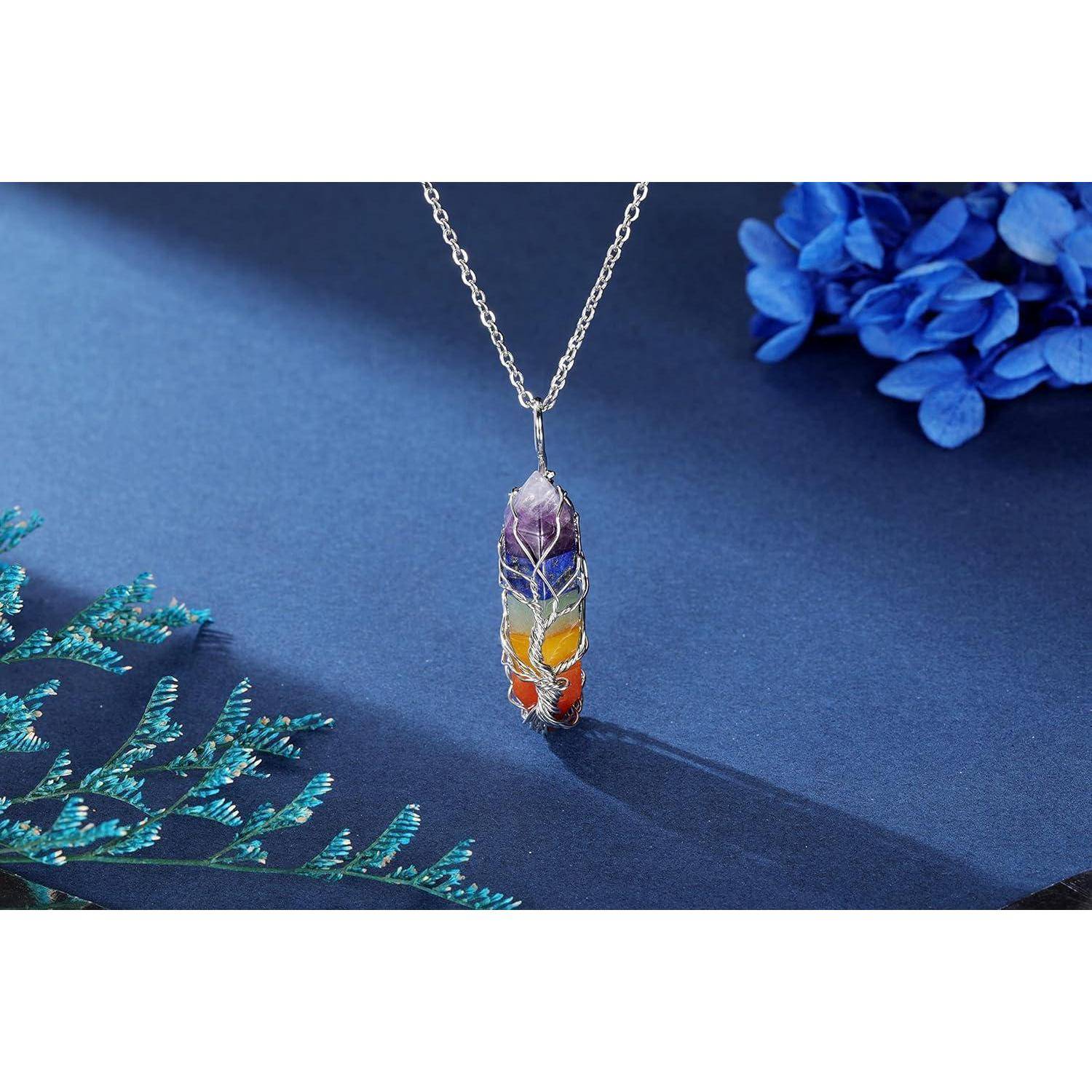 Eine farbenfrohe Kristallanhänger, in Silberdraht gewickelt, hängt an einer Kette und ruht auf einer blauen Oberfläche mit dekorativen Blumen in der Nähe.
