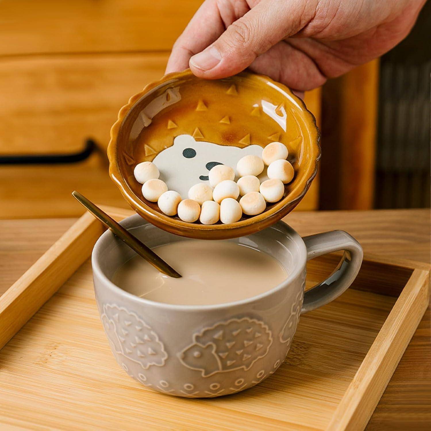 Eine Hand gießt kleine, runde, weiße Süßigkeiten aus einer bärchenförmigen Schüssel in eine Tasse Milchtee. Die Tasse hat ein Igeldesign.