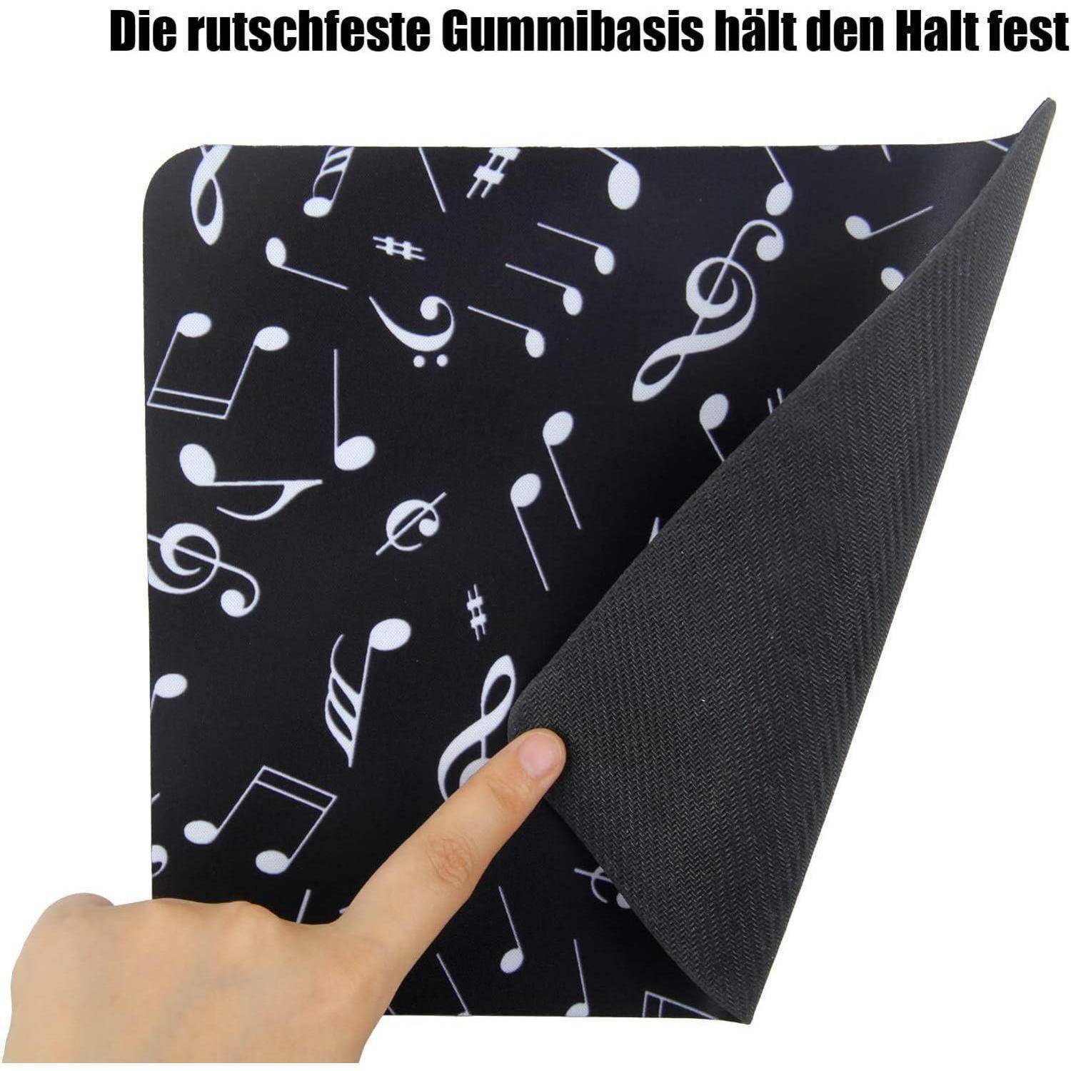 Eine Hand hält eine schwarze Matte mit weißem Musiknoten-Design, eine Ecke ist angehoben, um die rutschfeste Gummibasis zu zeigen. Text auf Deutsch liest: Die rutschfeste Gummibasis hält den Halt fest.