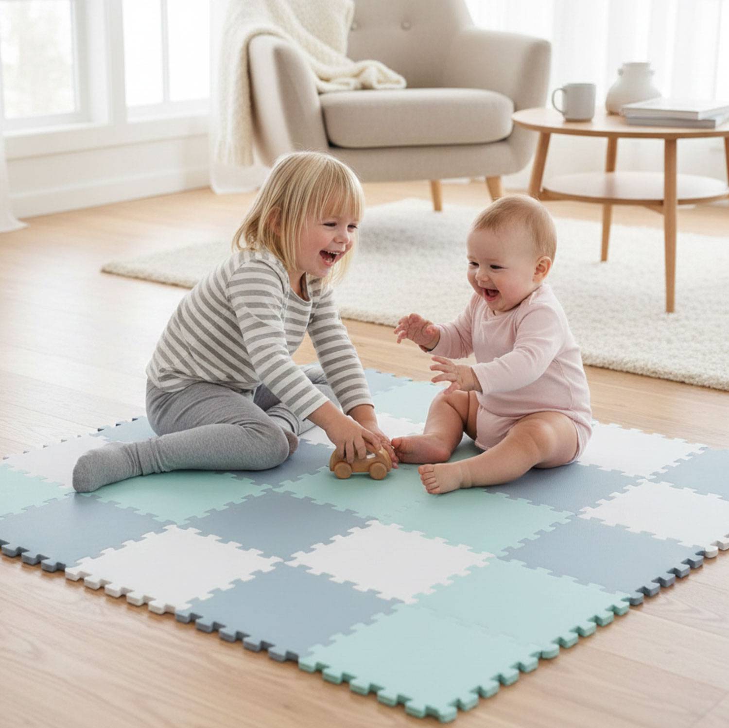 Ein Kleinkind und ein Baby spielen auf einer blauen und weißen Schaumstoffmatte in einem hellen Raum, wobei im Hintergrund ein Stuhl und ein Fenster zu sehen sind.