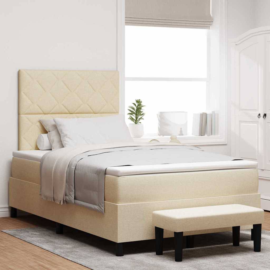 Ein beiges Bett mit gepolstertem Kopfteil, bezogen mit weißer und grauer Bettwäsche, steht zentral in einem hellen Raum mit zwei Fenstern und einer kleinen Bank.