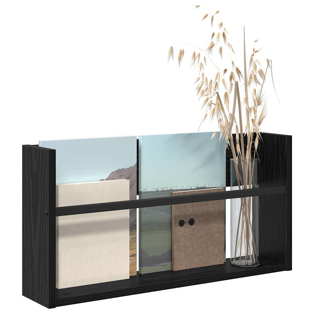 Ein schwarzes Holzregal mit gerahmten Bildern und einer hohen Glasvase mit getrockneten Gräsern, die eine minimalistische dekorative Anordnung bilden.