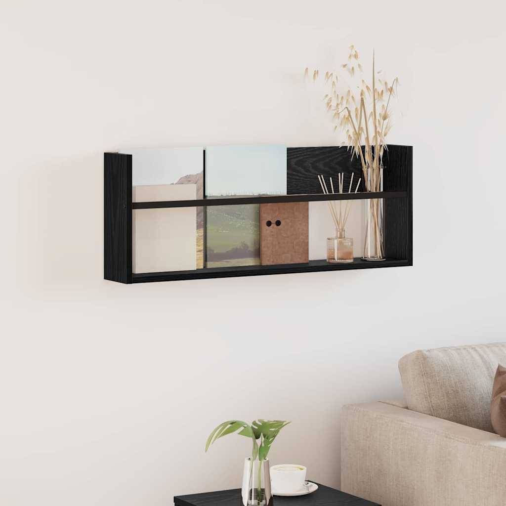 Ein kleines schwarzes Wandregal trägt Bücher, Vasen und Dekorationsgegenstände. Ein beiges Sofa ist teilweise darunter sichtbar. Minimalistische Einrichtung.