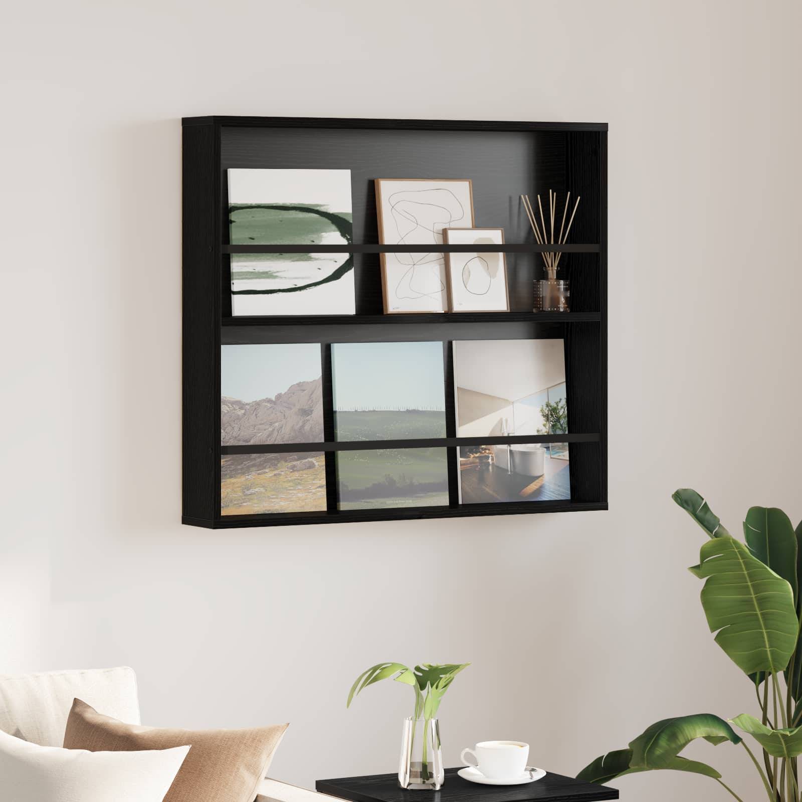 Ein schwarzes Wandregal zeigt abstrakte Kunstwerke, einen Schilfstäbchendiffuser und gerahmte Landschaftsfotos. Darunter befindet sich ein Sofa und eine Topfpflanze.