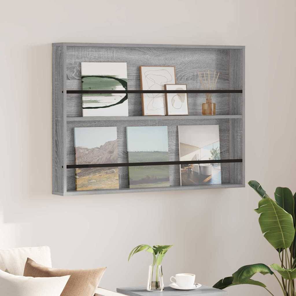 Ein grauer wandmontierter Regalträger zeigt gerahmte abstrakte Kunst, einen Schilfstäbchendiffusor und kleine Dekorationsgegenstände. Eine Pflanze in einem Topf befindet sich in der Nähe.