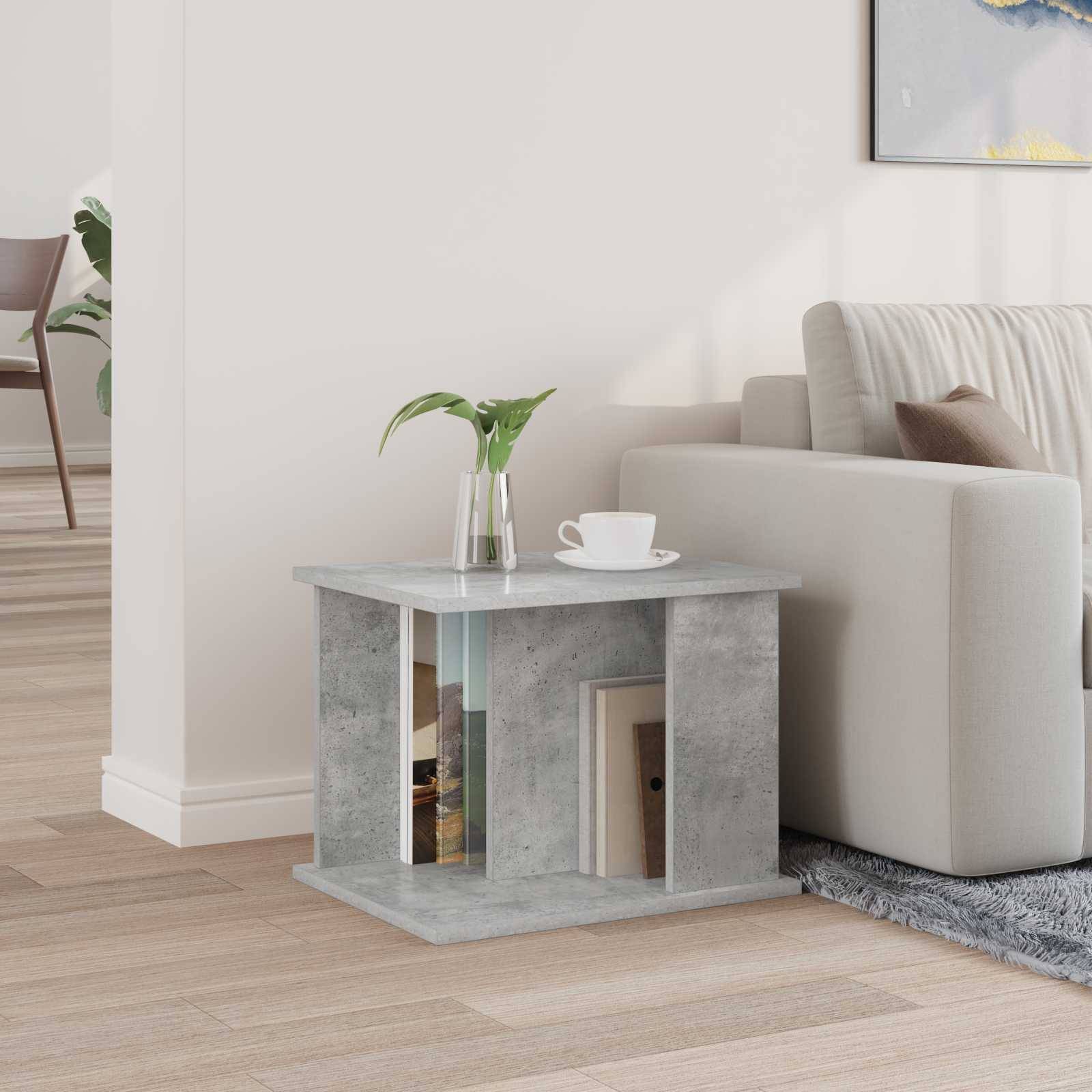 Ein modernes Wohnzimmer mit einem grauen Sofa und einem kleinen quadratischen Beistelltisch. Auf dem Tisch steht eine Vase mit Grünpflanzen und einigen Büchern. Ein teilweiser Blick auf ein Kunstwerk an der Wand ist zu sehen.