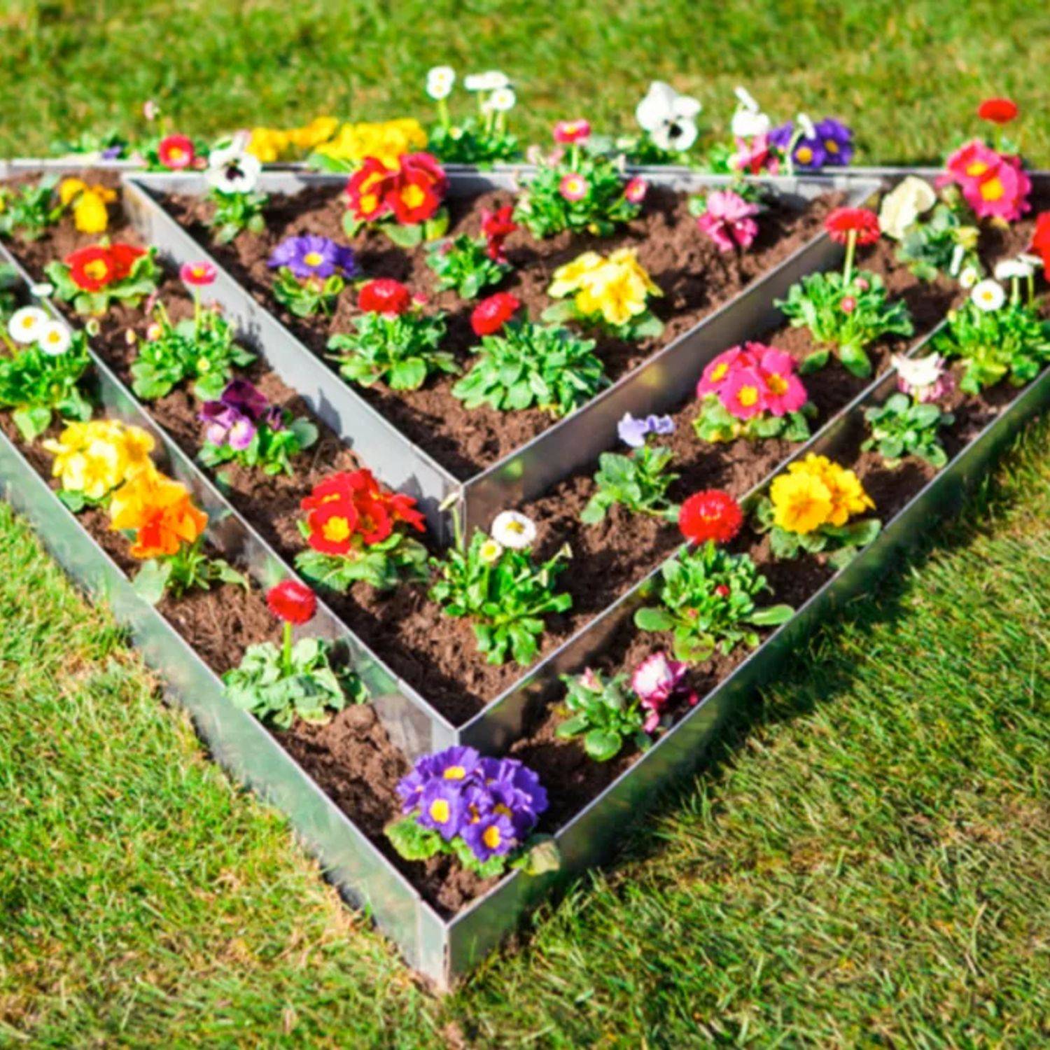 Ein dreieckiges erhöhtes Hochbeet mit bunten Blumen, darunter rote, gelbe, lila und weiße Blüten, in ordentlichen Reihen auf Rasen angeordnet.