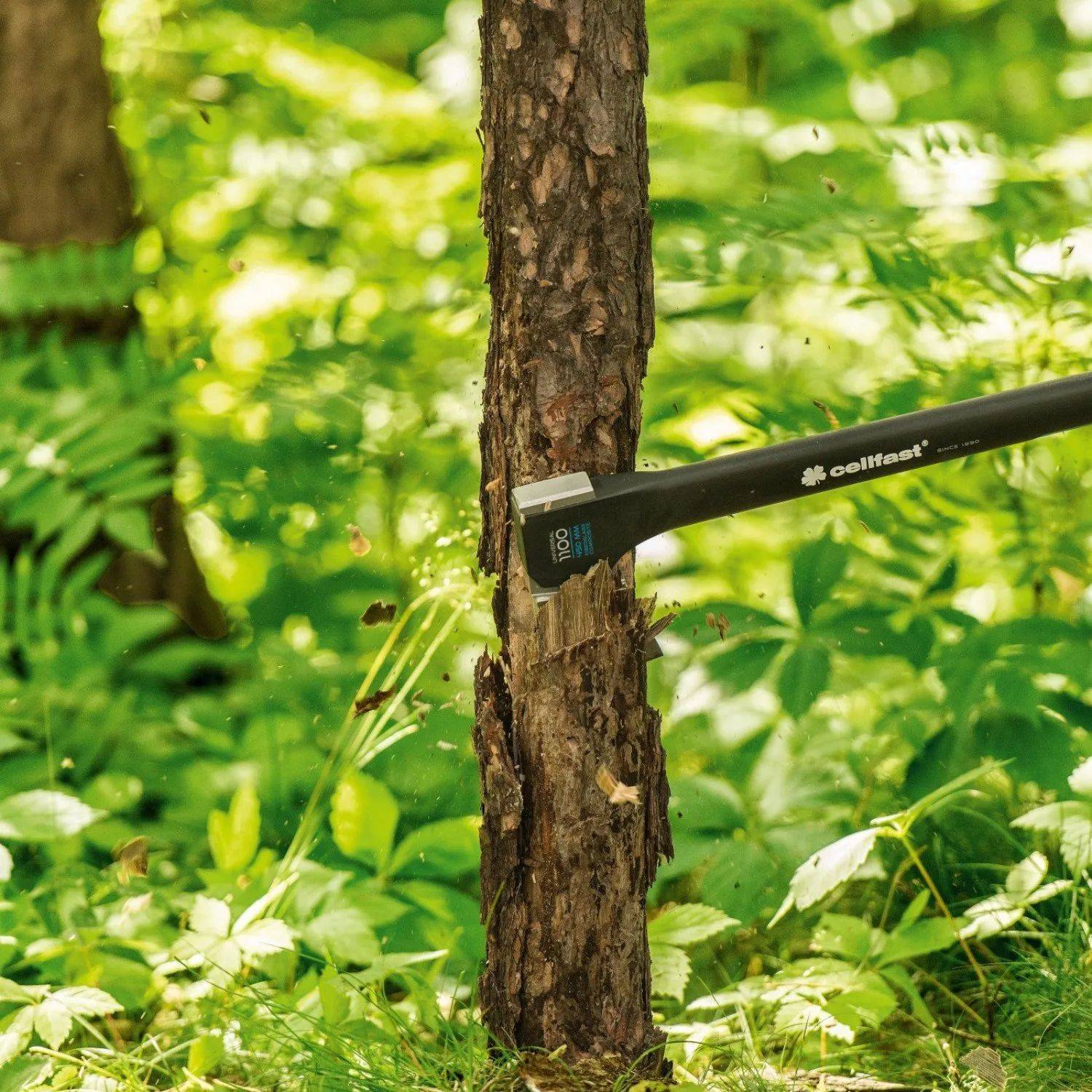 Eine Axt, die in den Stamm eines Baumes in einer Waldlandschaft eingeschlagen ist, umgeben von grünem Blattwerk. Die Szene deutet auf Holzfäller-Arbeit in einer natürlichen Umgebung hin.