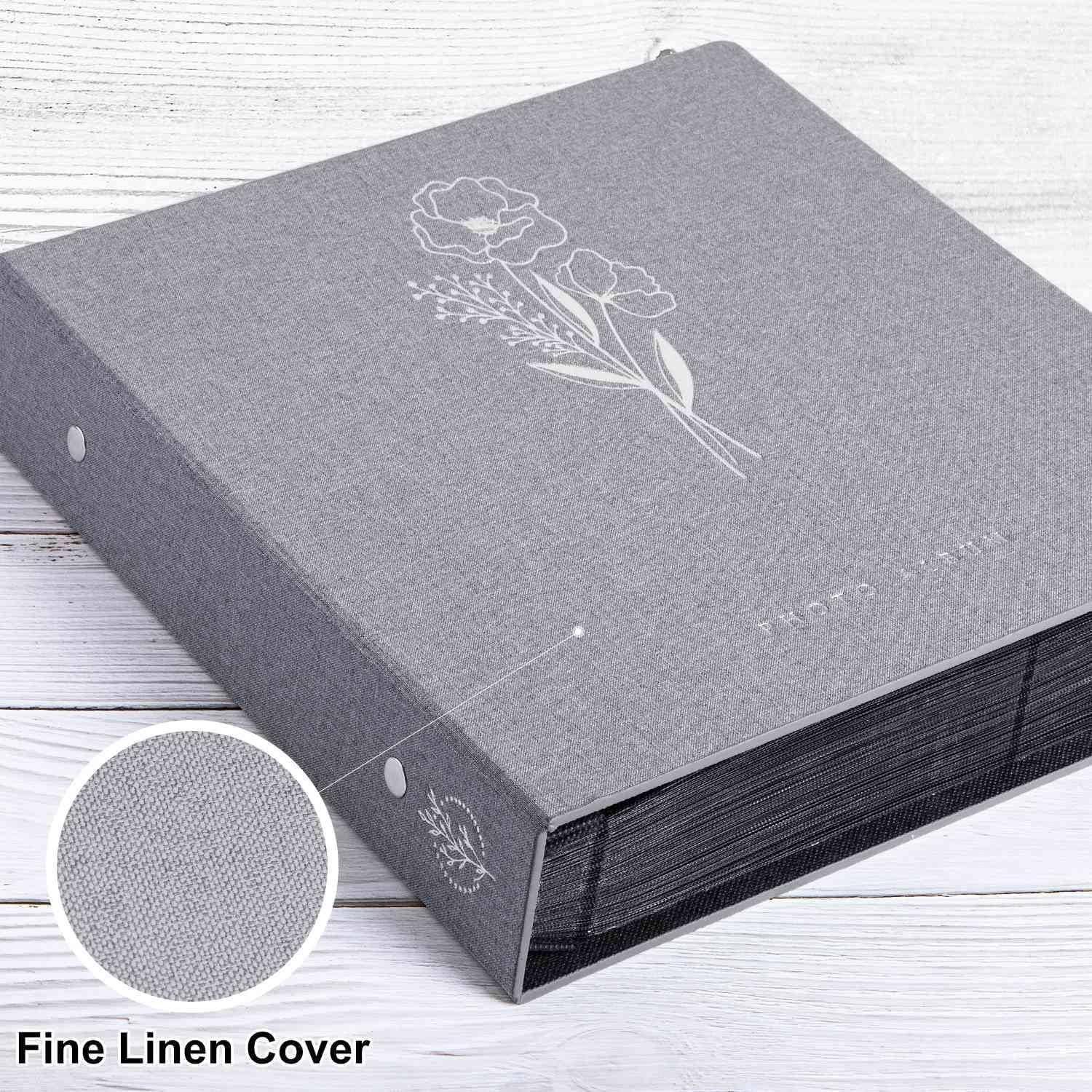 Graues Fotoalbum mit weißem Blumendesign und Etikett 'Fine Linen Cover', das auf einer hellen Holzoberfläche liegt.