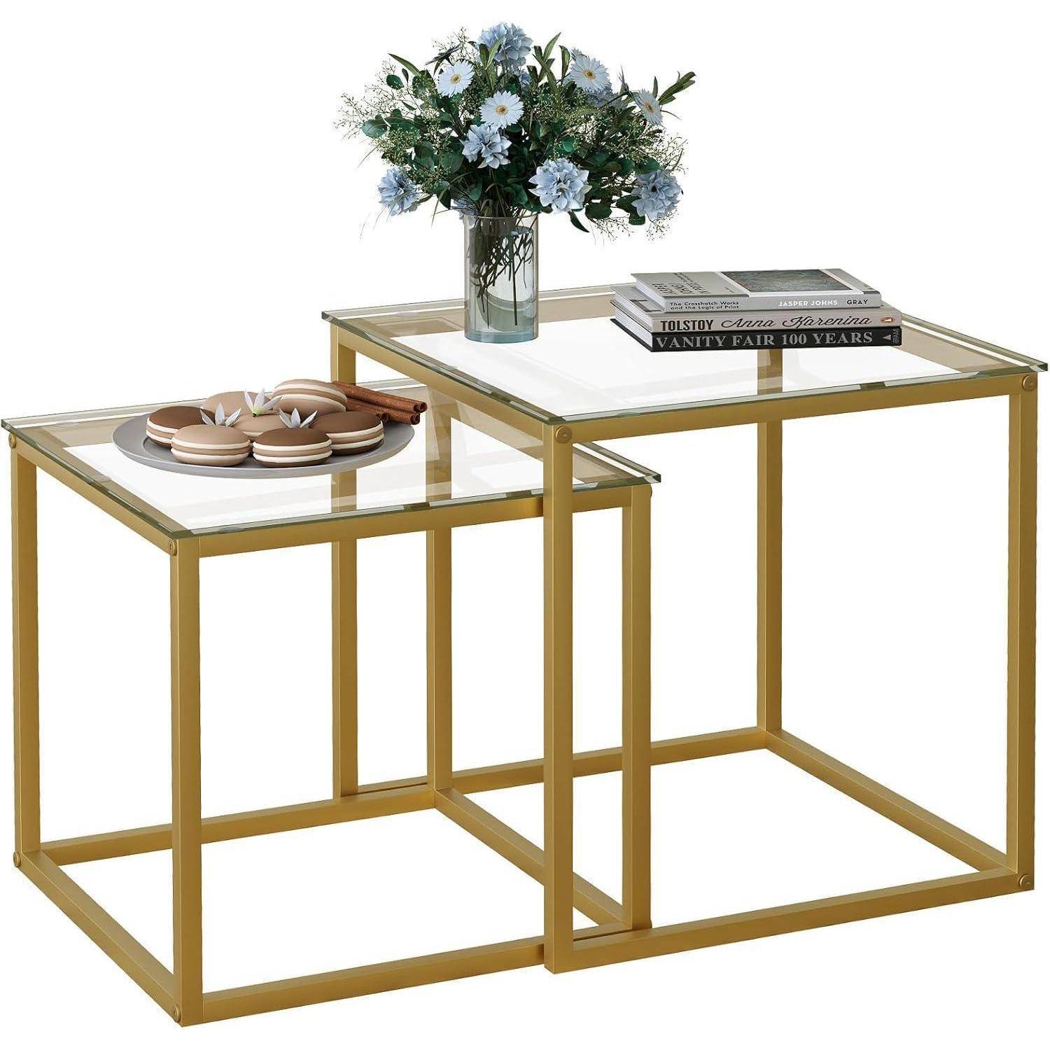 Verschachtelte Tische mit goldenen Rahmen, Glasplatten; ein Tisch trägt eine Vase mit Blumen, der andere beherbergt Bücher und Dekorationsgegenstände.