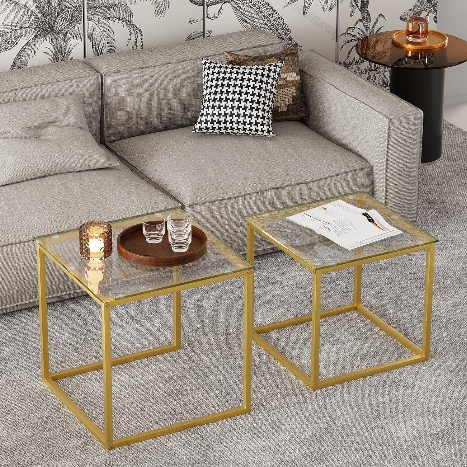 Ein modernes Wohnzimmer präsentiert ein graues Sofa mit einem schwarz-weißen gemusterten Kissen, einem dekorativen Wandhintergrund und zwei Glastischen mit goldenem Metallgestell.