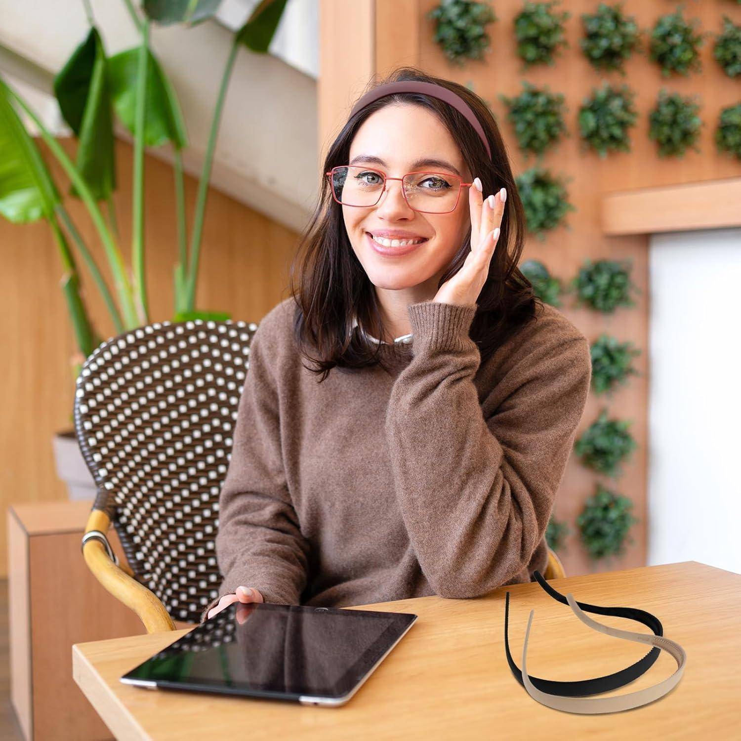 Eine Person sitzt an einem Tisch mit einem Tablet, lächelt und macht eine Telefongebärde. Grüne Pflanzen befinden sich im Hintergrund an einer Holzwand.