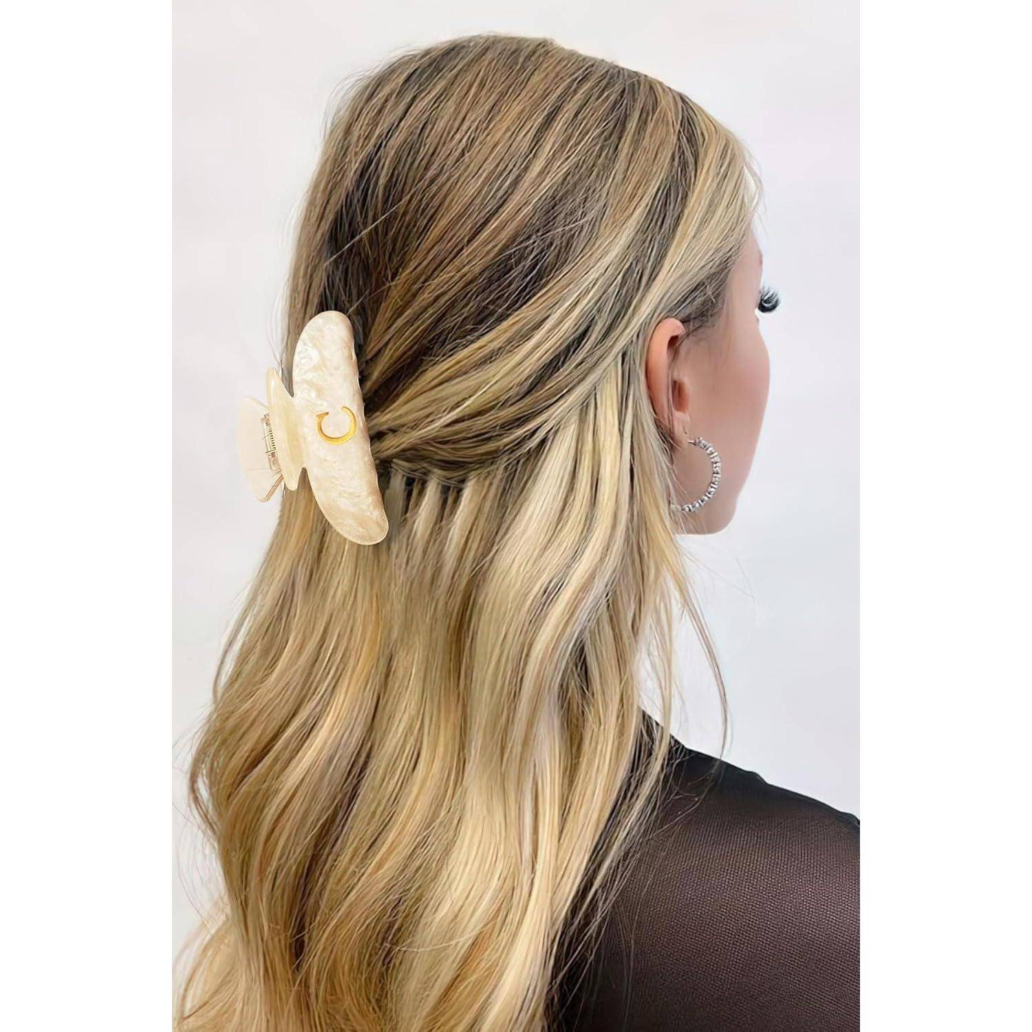 Eine Frau mit langen, blonden Haaren steht seitlich, trägt ein schwarzes Oberteil. Eine große, hellfarben Haarspange hält ihre Haare zusammen.