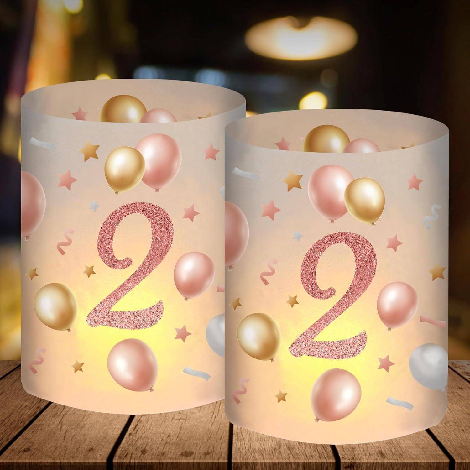 Ein Paar leuchtende Kerzenhalter mit der Zahl '2', rosafarbenen und goldenen Luftballons sowie Sternen. Auf einer Holzoberfläche vor einem unscharfen Hintergrund platziert.
