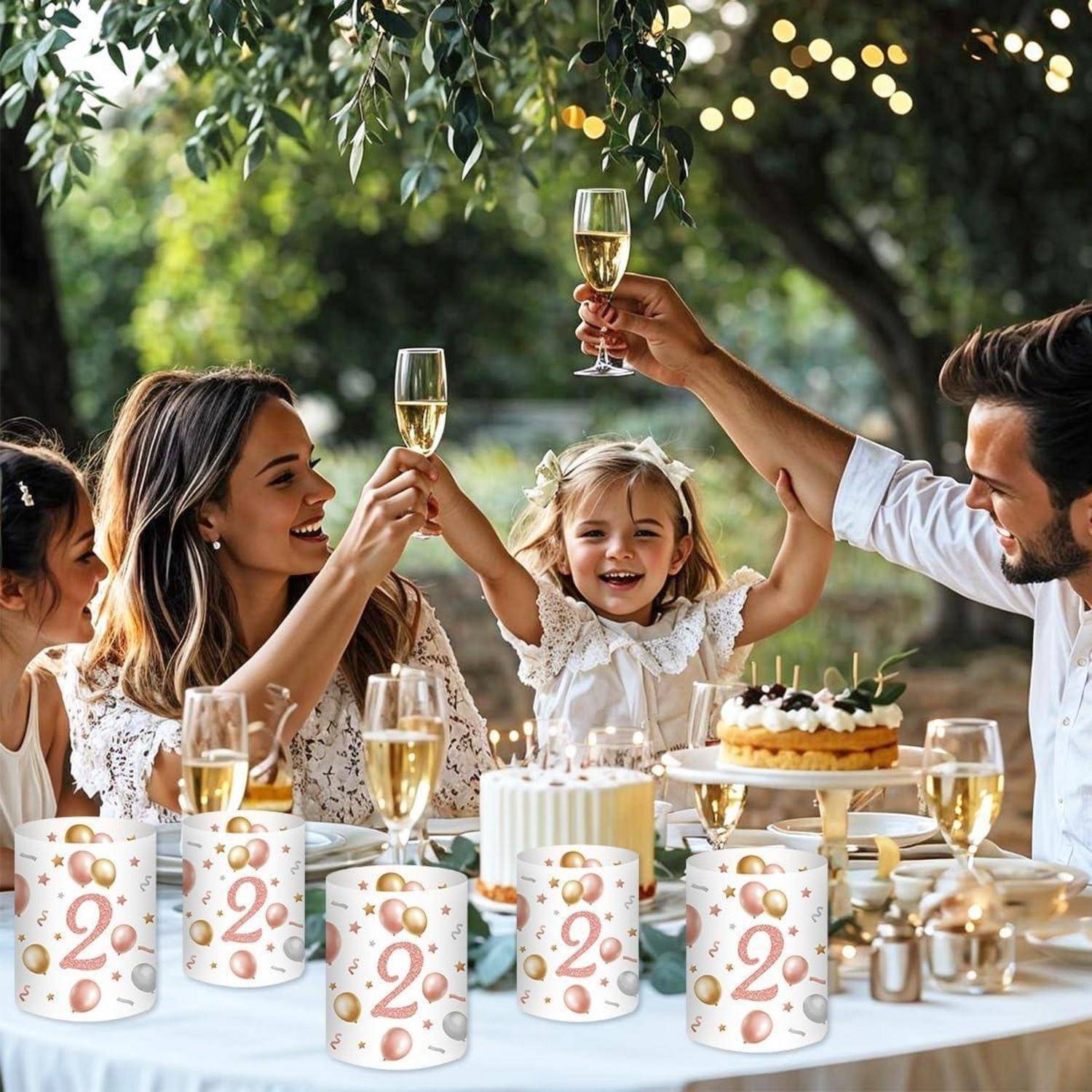 Eine vierköpfige Familie stößt mit Champagner bei einer Geburtstagsfeier im Freien an. Im Vordergrund steht ein Tisch mit einer Torte, Kerzen und festlicher Dekoration.