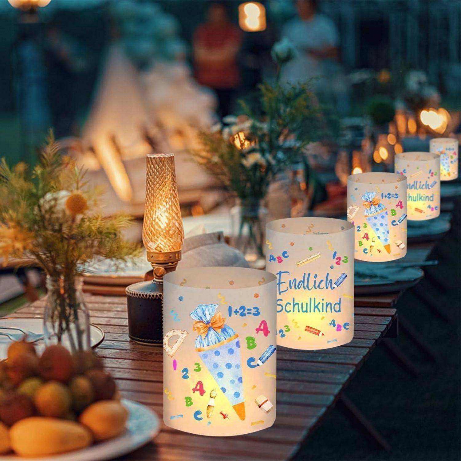 Ein festlich geschmückter Outdoor-Tisch in der Abenddämmerung mit leuchtenden Laternen, auf denen der Text ‚Endlich Schulkind' und schulthematische Illustrationen zu sehen sind.