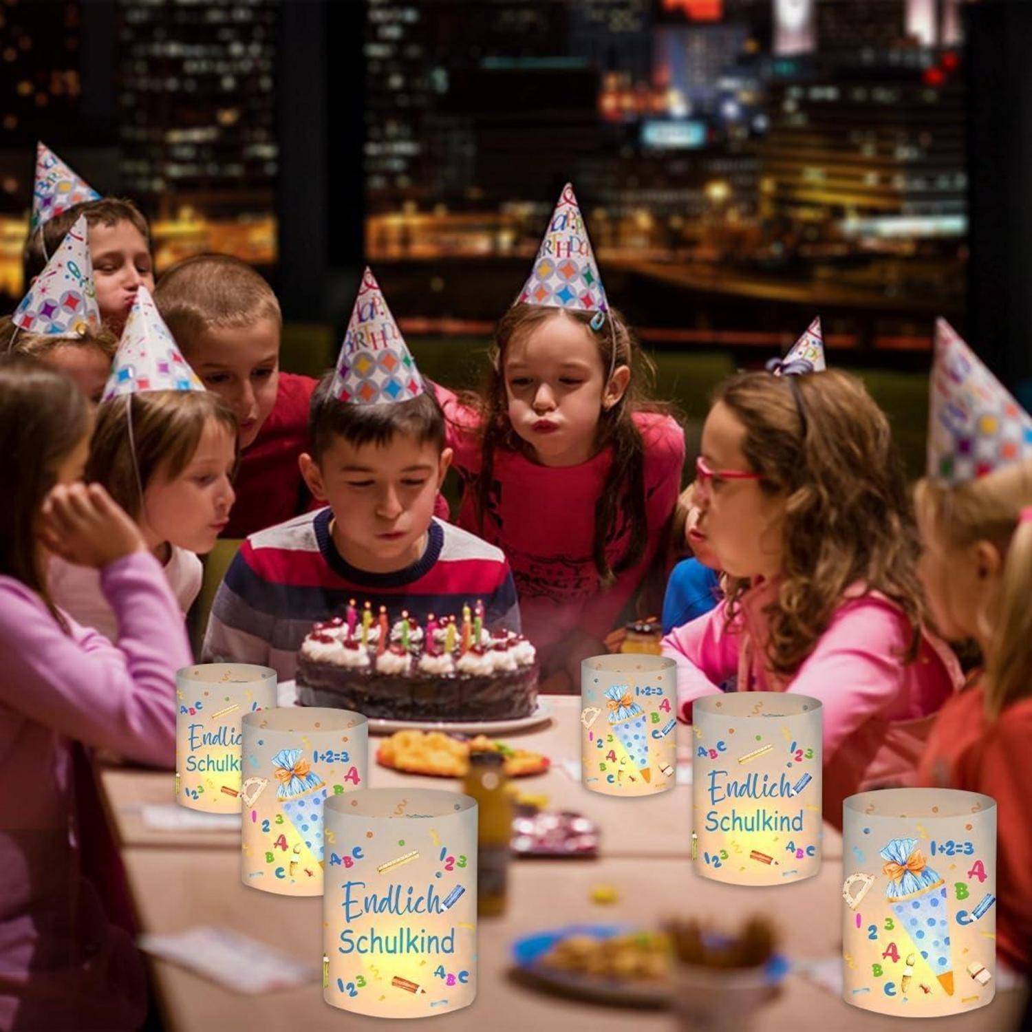 Kinder auf einer Geburtstagsfeier tragen festliche Hüte und sind um einen Kuchen mit brennenden Kerzen versammelt. Geschenktüten auf dem Tisch tragen die Aufschrift „Endlich Schulkind