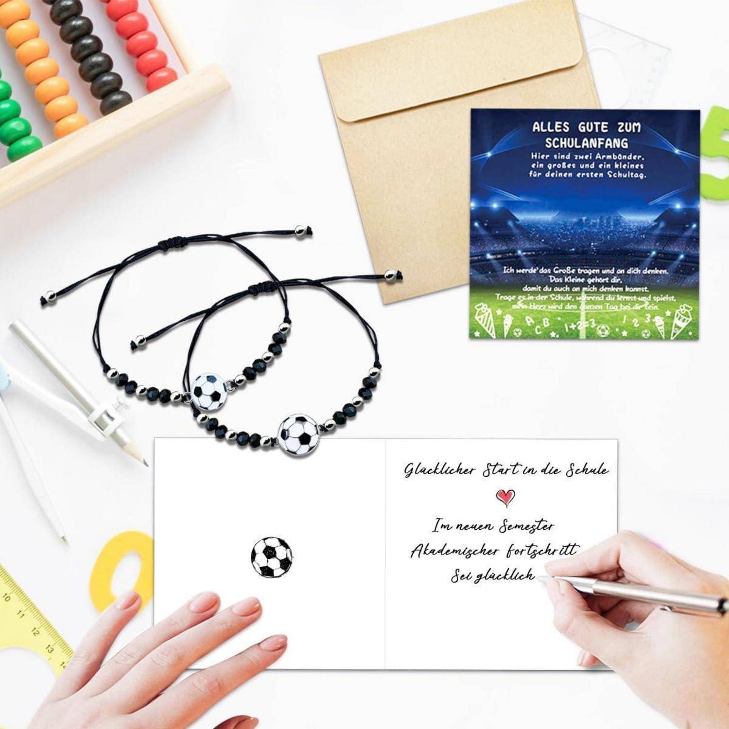 Ein Schreibtisch mit Schulmaterialien, eine Grußkarte mit handgeschriebenem Vermerk ‚Glücklicher Start in die Schule' und Fußball-Armbänder.