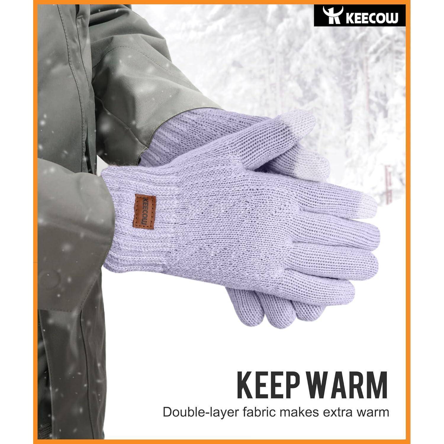 Eine Person in einer grünen Jacke trägt Lavendel-Handschuhe mit einem Etikett und steht im Schnee. Der Text lautet: 