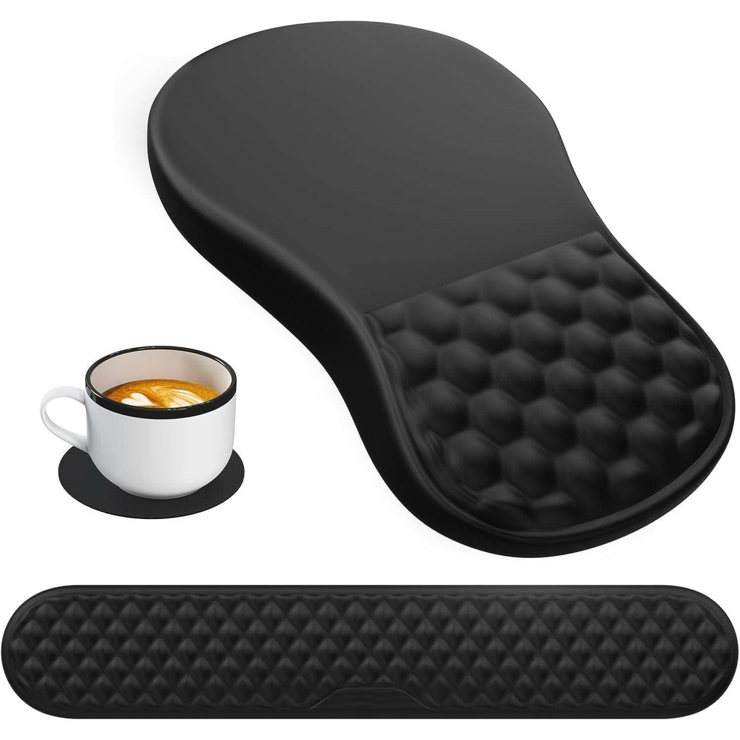 Ein schwarzes ergonomisches Mauspad mit einer strukturierten Handgelenkauflage neben einer Untertasse und einer Tasse Kaffee mit Latte-Art, was auf Arbeit oder Freizeit hindeutet.