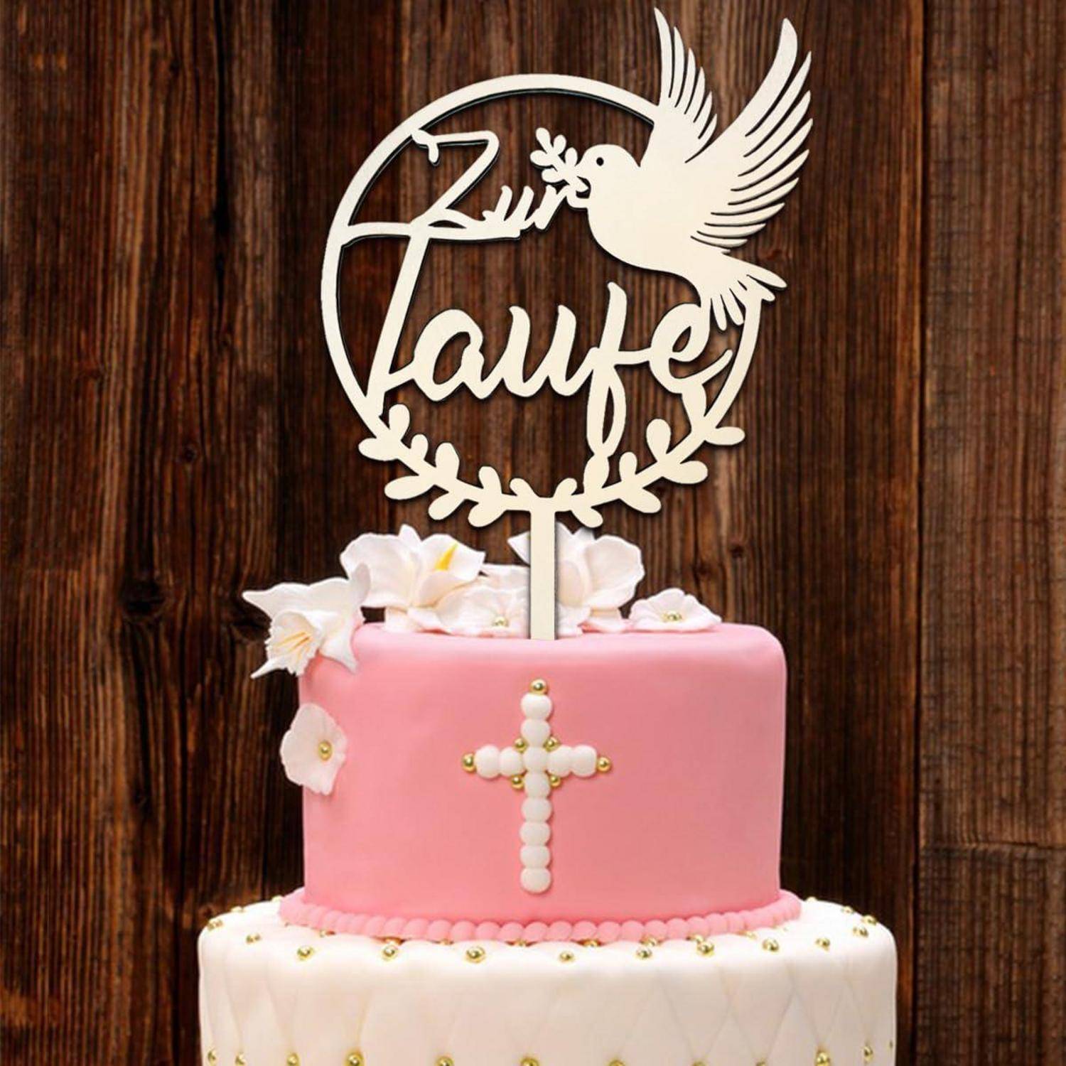 Rosa und weiße Torte mit einem Kreuz-Detail, oben mit weißen Blumen und einer Dekoration mit einer Taube und dem Wort ‚Taufe'.