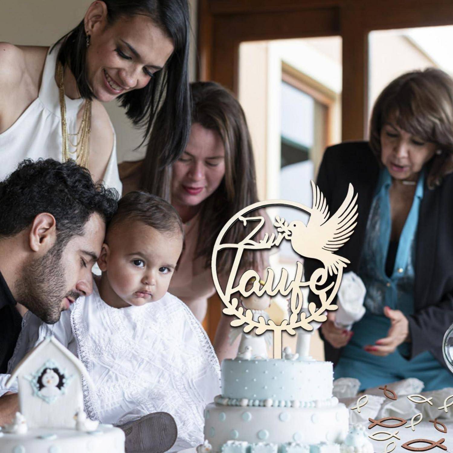 Eine Familie versammelt sich um eine dekorierte Torte bei einer Tauffeier. Ein Baby in Weiß wird von einem Mann gehalten, umgeben von lächelnden Erwachsenen.
