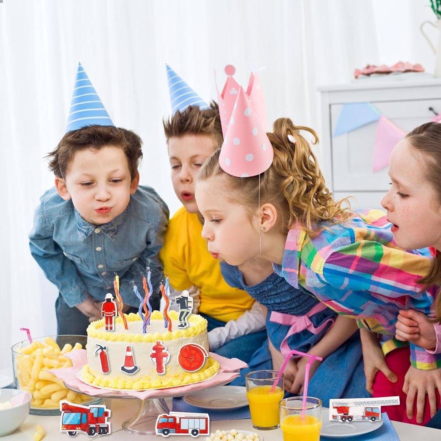 Kinder mit Partyhüten versammeln sich um einen Tisch mit einer Geburtstagstorte und Snacks. Die Torte ist mit dekorativen Feuerwehrautos verziert.