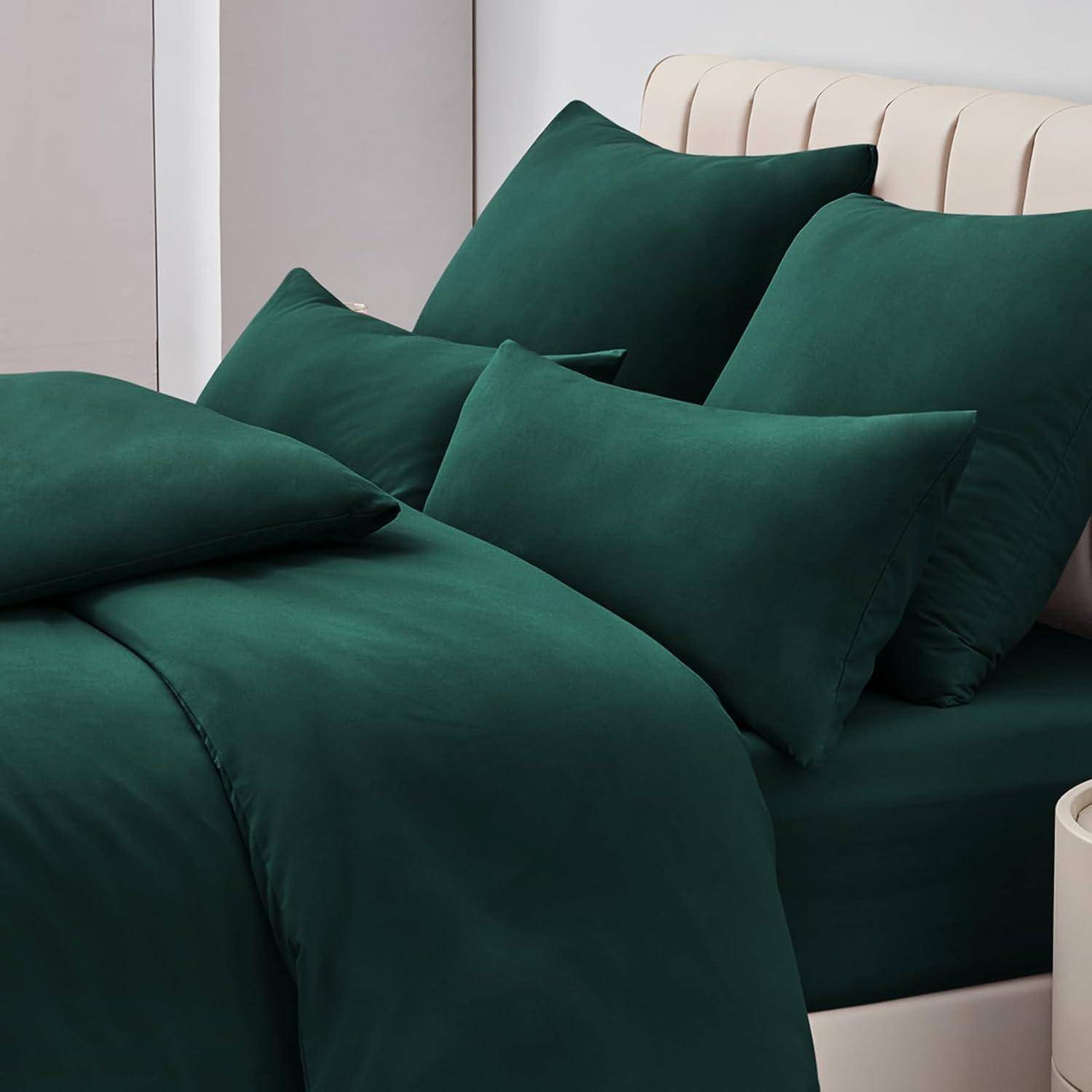 Ein sorgfältig gemachtes Bett mit dunkler Grünbettwäsche und mehreren Kissen ist in einer hellgefärbten Raumecke zu sehen.