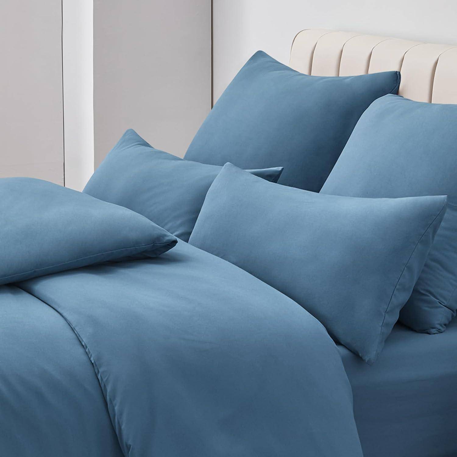 Ein ordentlich gemachtes Bett mit blauen Kissen, Bettwäsche und einer Bettdecke, vor einem teilweise sichtbaren hellfarben Kopfteil und einer Wand.