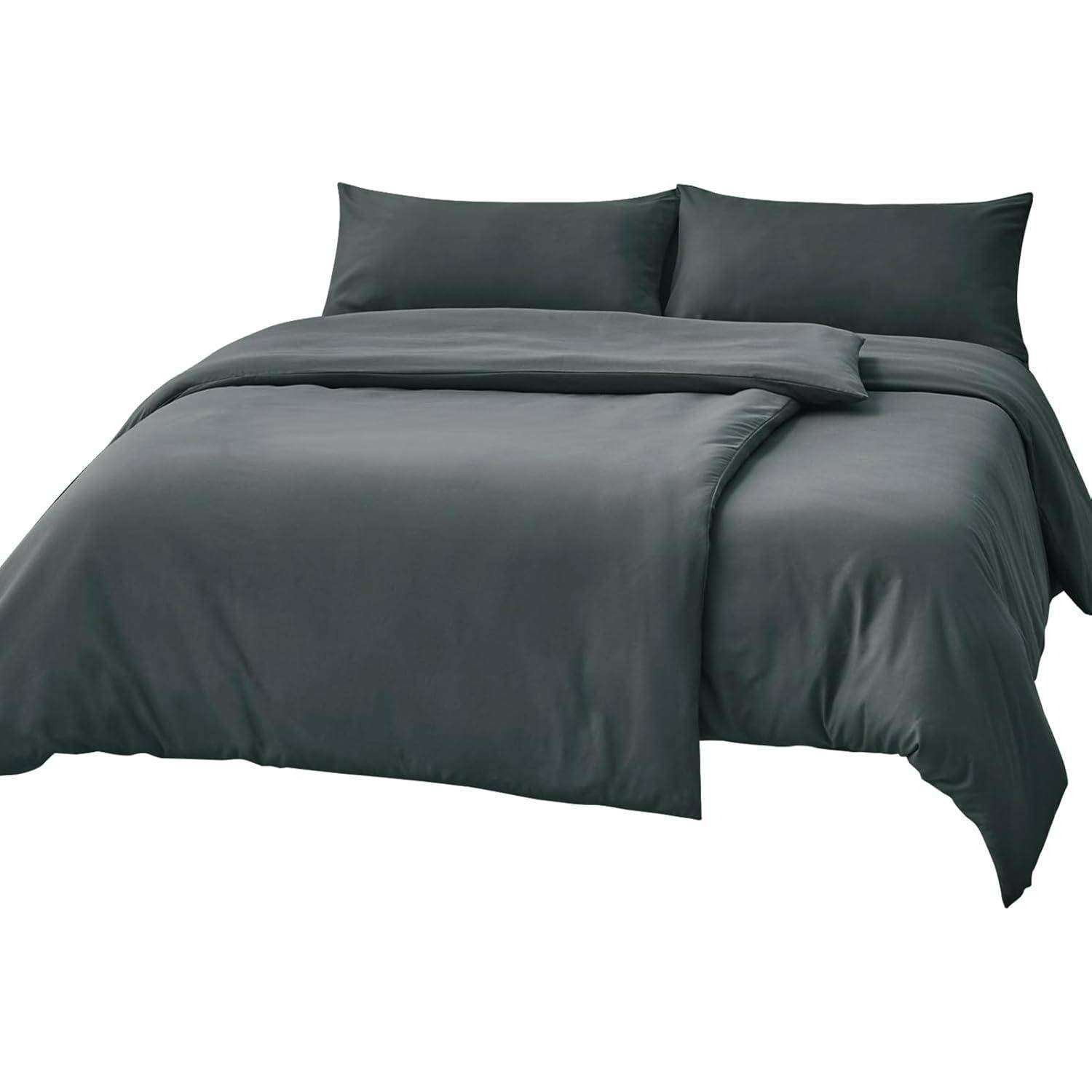 Ein ordentlich gemachtes Bett mit einem dunkelgrauen Bettüberwurf und zwei passenden Kissen, das einen minimalistischen und modernen Eindruck vermittelt.