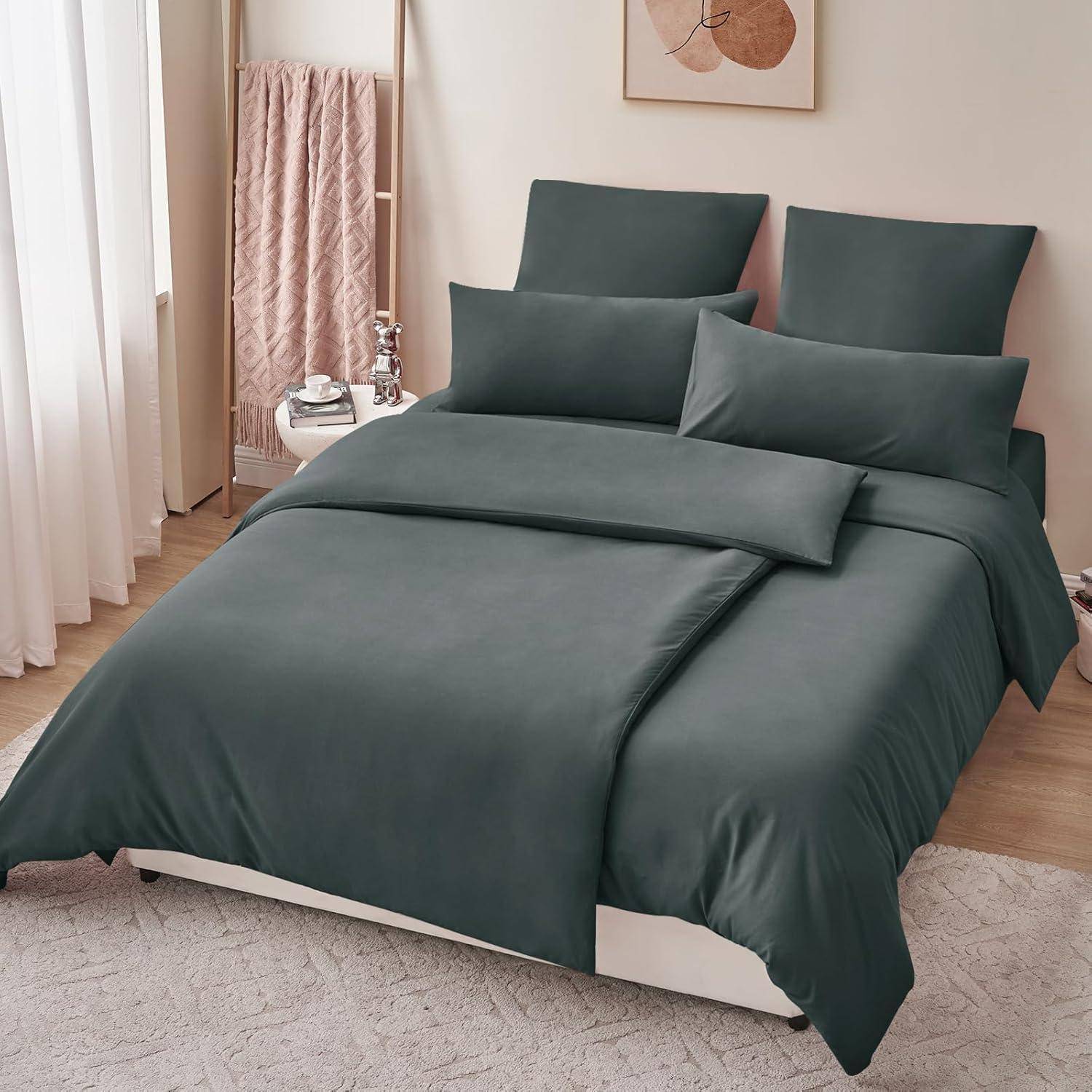 Ein ordentlich gemachtes Bett mit dunkelgrauer Bettwäsche, einschließlich Kissen und Bettdecke. Ein Handtuchhalter und abstrakte Wandkunst sind im Hintergrund zu sehen.