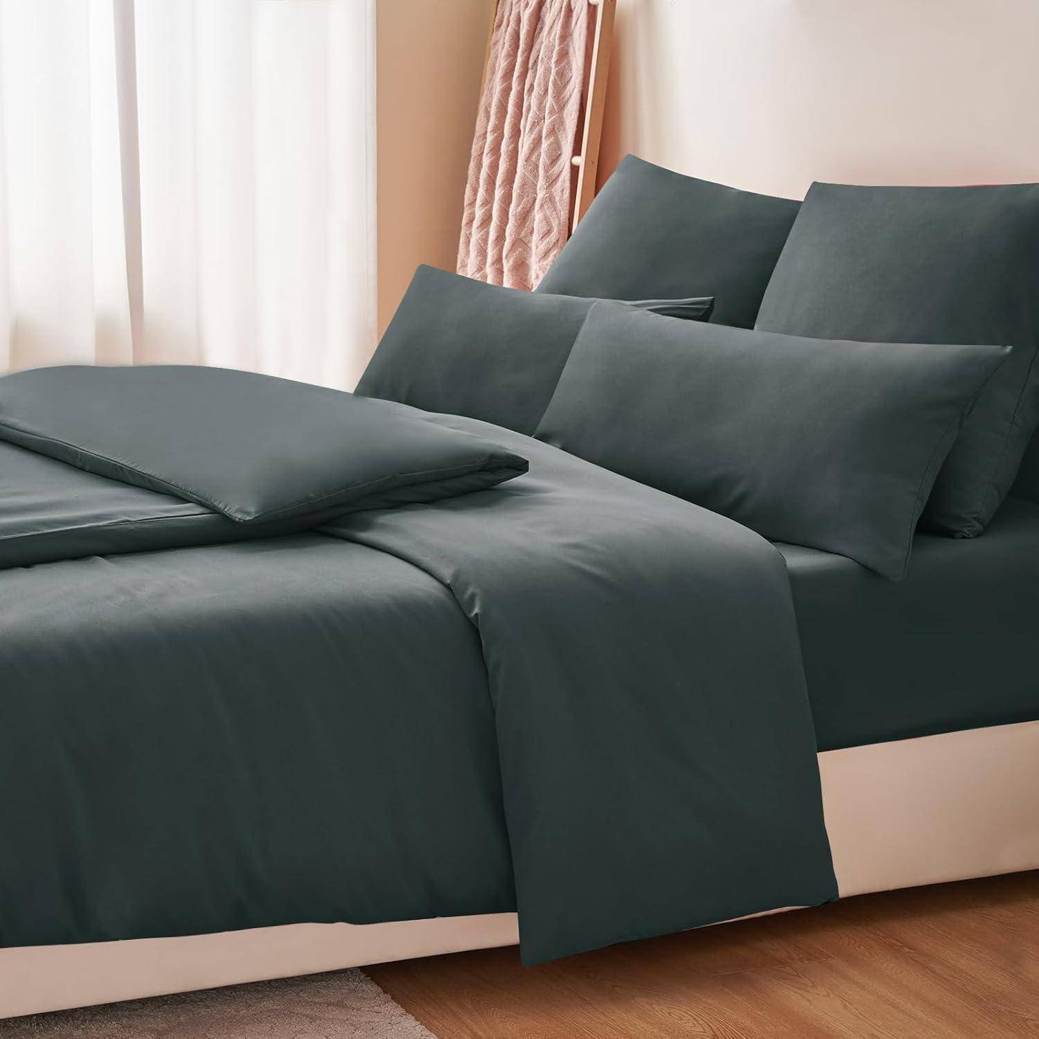 Ein ordentlich gemachtes Bett mit dunklen Grünlaken, Kissen und Bettdecke in einem sonnigen Raum, mit einem beigen Kopfteil und teilweise sichtbarem Vorhang.