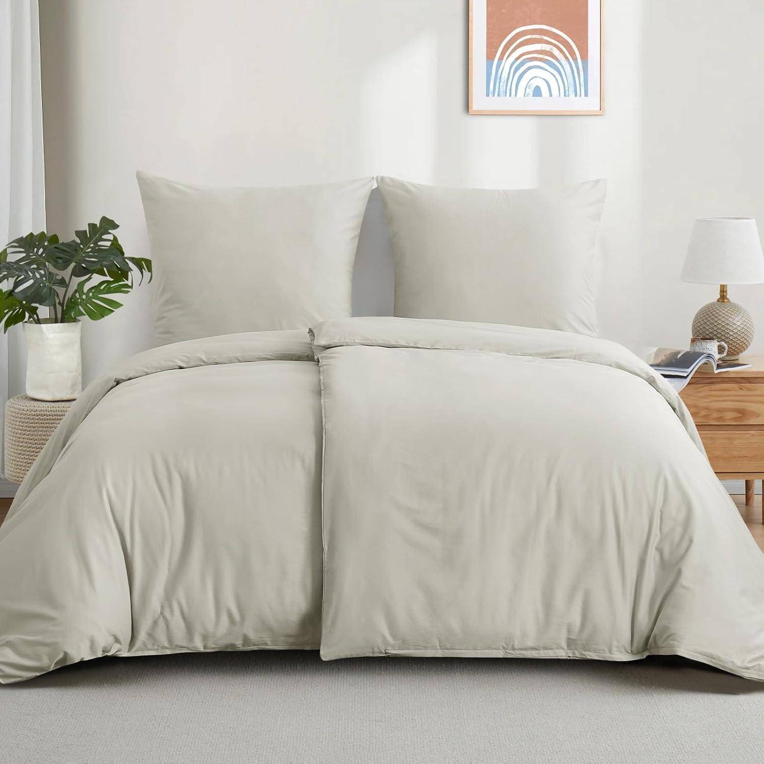 Ein ordentlich gemachtes Bett mit hellgrauer Bettwäsche in einem minimalistischen Raum. Pflanzen, eine Lampe und ein gerahmter Regenbogendruck verleihen der Dekoration dezente Akzente.