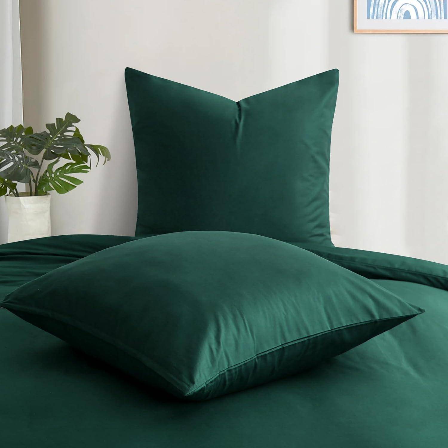 Ein Bett mit dunkelgrünen Kissen und Bettwäsche, neben einer weißen Wand und einer Pflanze in einem weißen Topf, die eine ruhige Schlafzimmeratmosphäre schaffen.