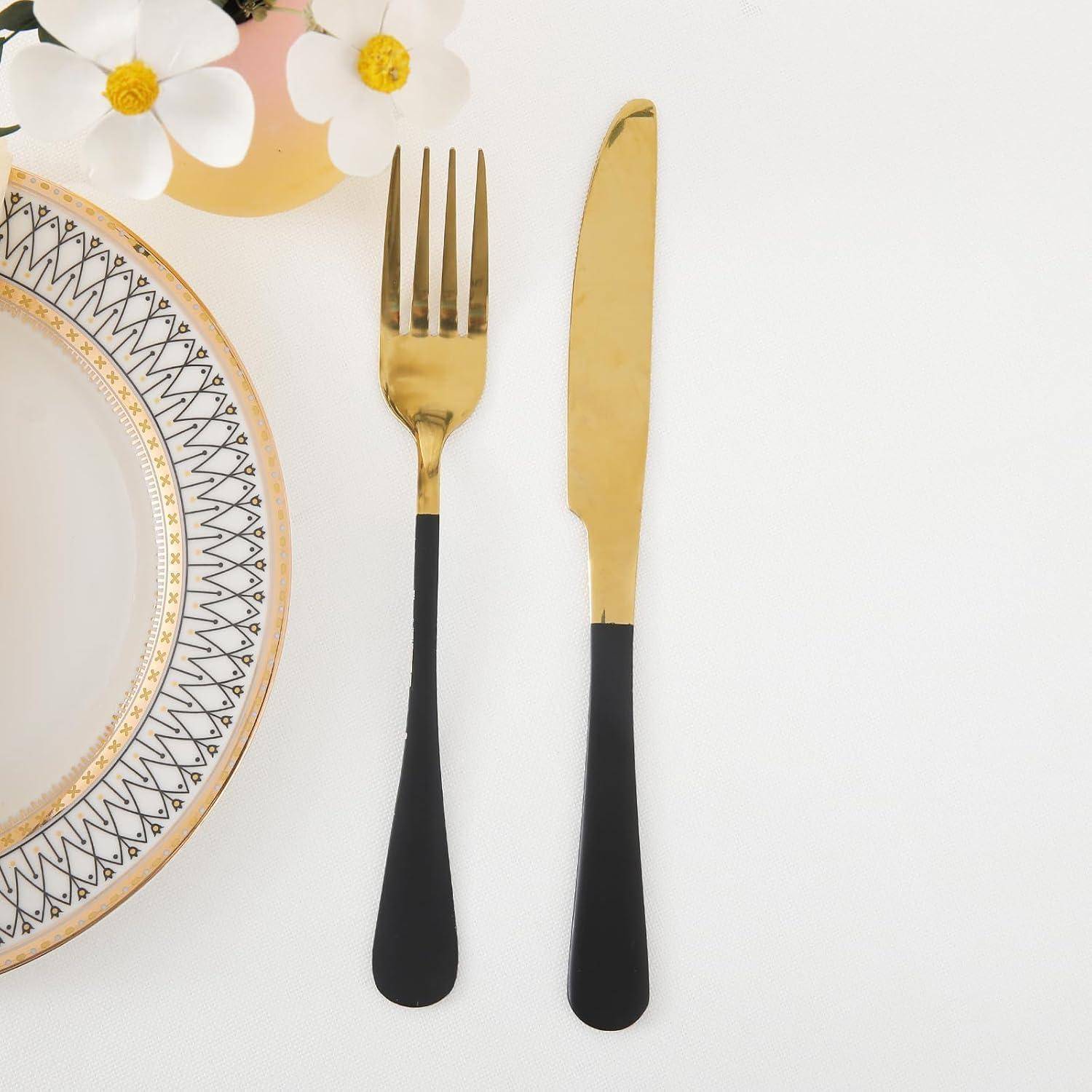 Ein dekoratives weißes Teller mit Goldmustern, eine Gabel und ein Messer mit Goldeinfassung und eine rosa Vase mit weißen Blumen auf einem weißen Tisch.