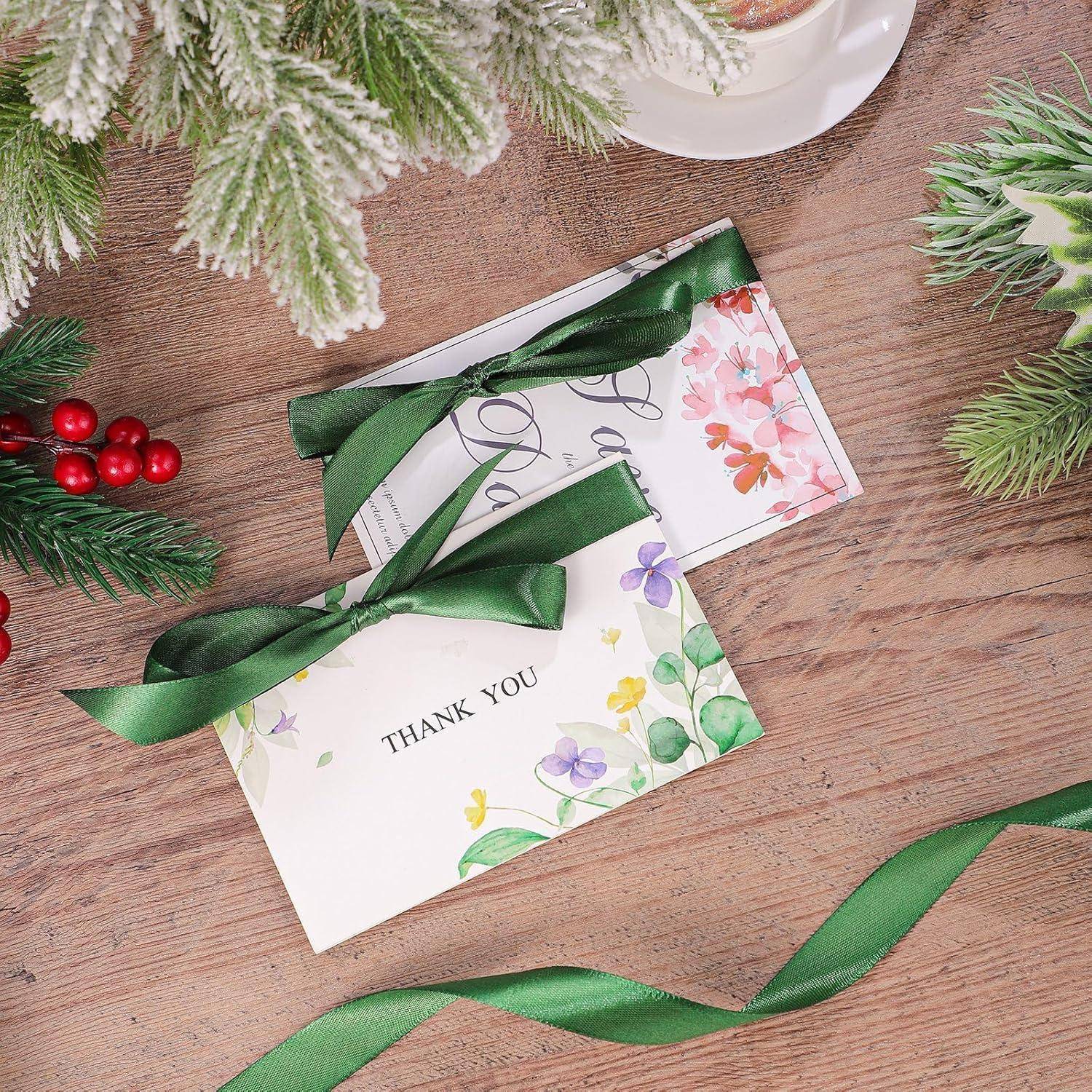 Weihnachtlich gestaltete Dankeskarten mit grünen Bändern und floralen Mustern auf einem Holztisch, umgeben von festlicher Grünpflanze und Beeren.