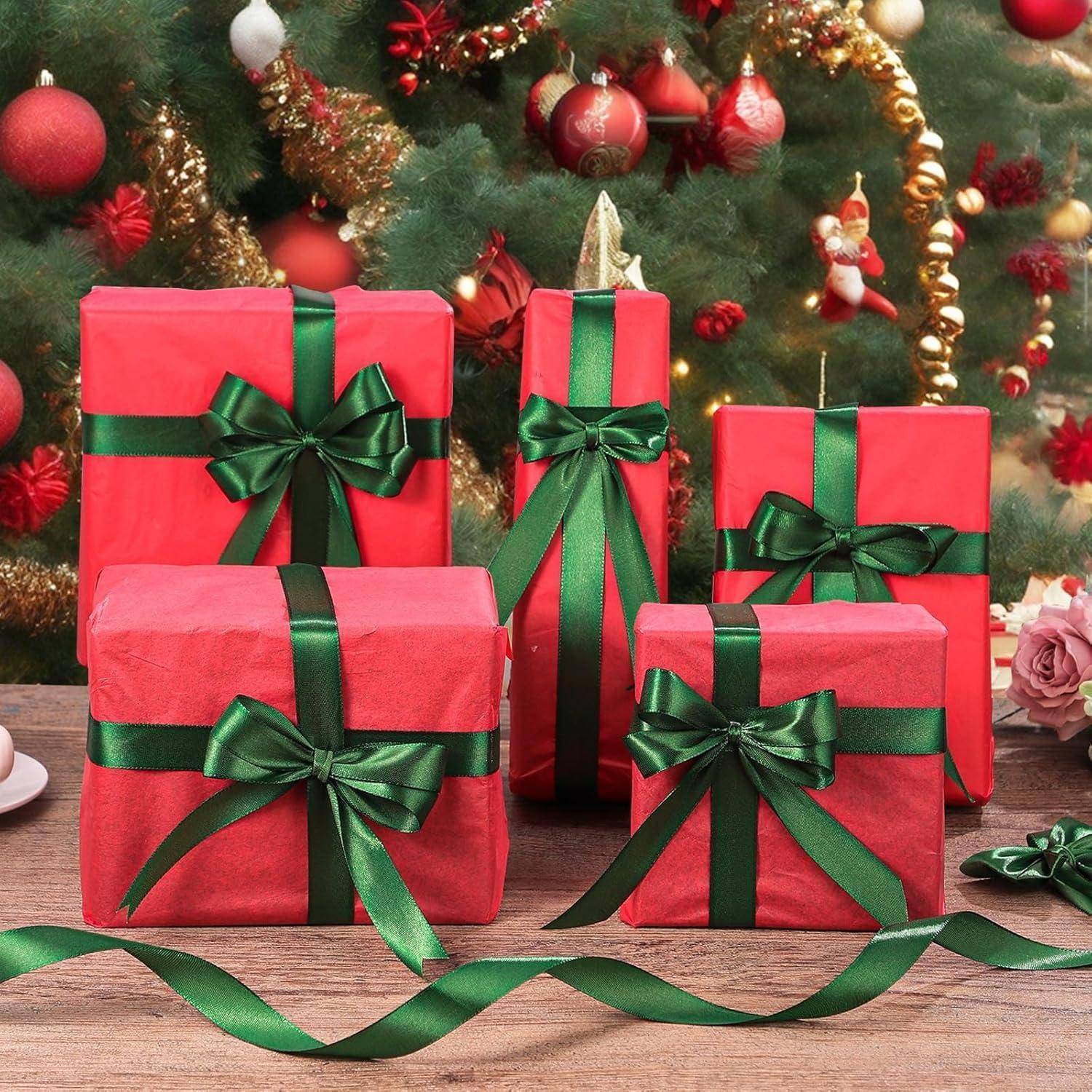 Rote Geschenkboxen mit grünen Bändern sind auf einem Tisch vor einem geschmückten Weihnachtsbaum angeordnet.