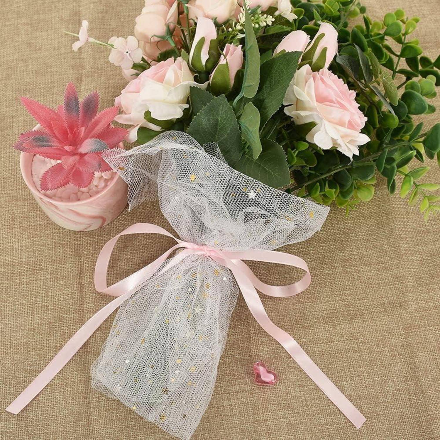 Ein Blumenstrauß aus rosa und weißen Rosen, und eine Spitzentasche mit einem rosa Band auf einer beigen Oberfläche. Eine kleine rosa Zierde ist in der Nähe.