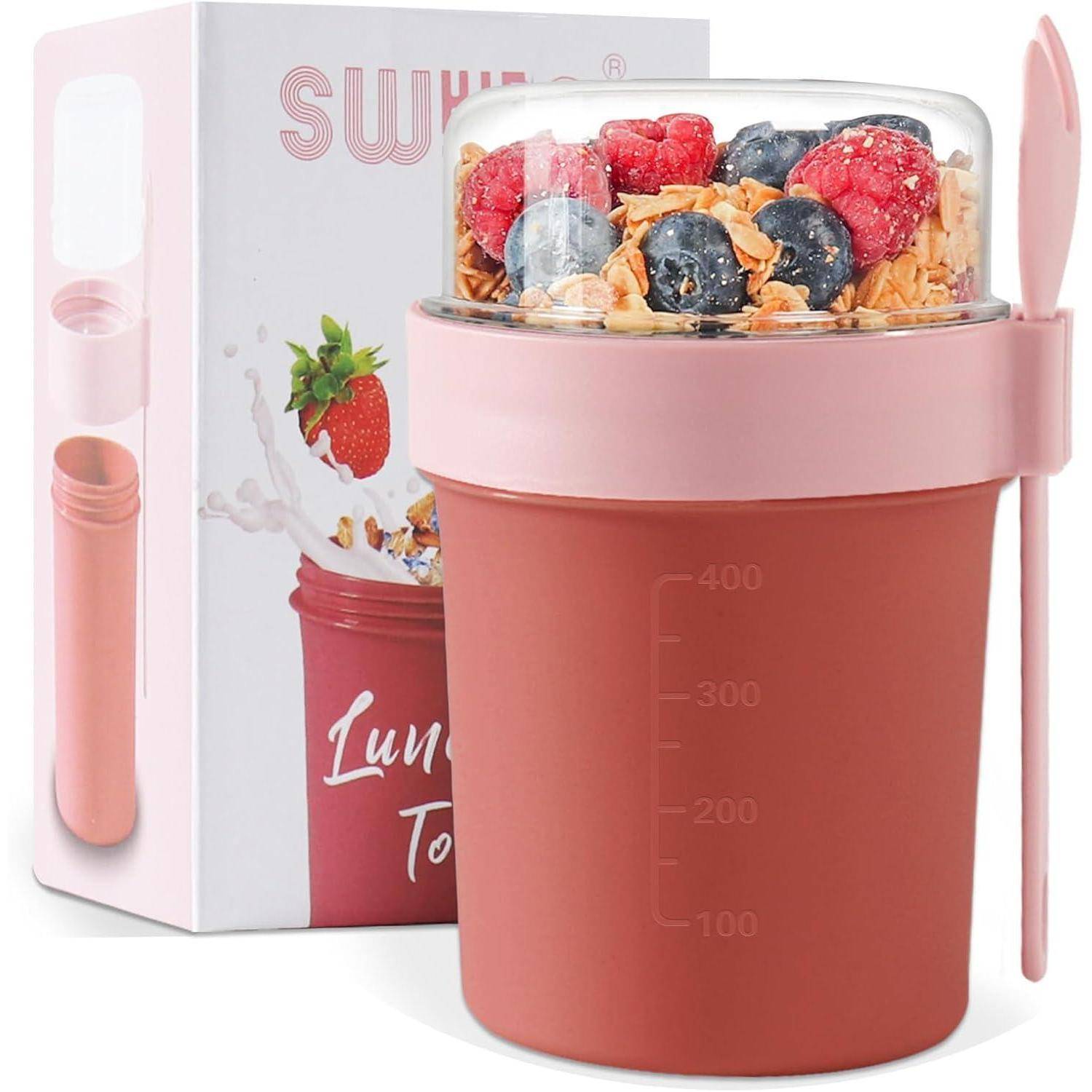 Ein rosa isolierter Behälter mit einem Löffel enthält Joghurt, der mit Granola und Beeren bedeckt ist. Die Box im Hintergrund zeigt ein Frucht- und Spritzdesign.