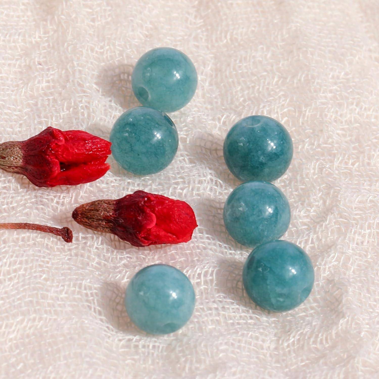 Blaue Perlen und getrocknete rote Blumen auf einer strukturierten weißen Oberfläche, zufällig angeordnet, zeigen den Kontrast zwischen leuchtenden Farben und einfachen Materialien.