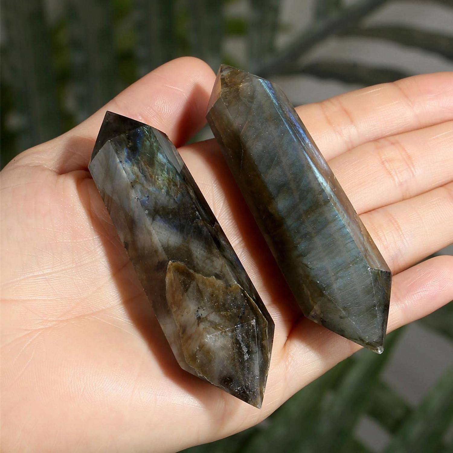 Eine Hand, die zwei polierte Labradorit-Steine hält, mit schillernden blauen und grünen Reflexionen, die ihre natürliche Schönheit hervorheben.