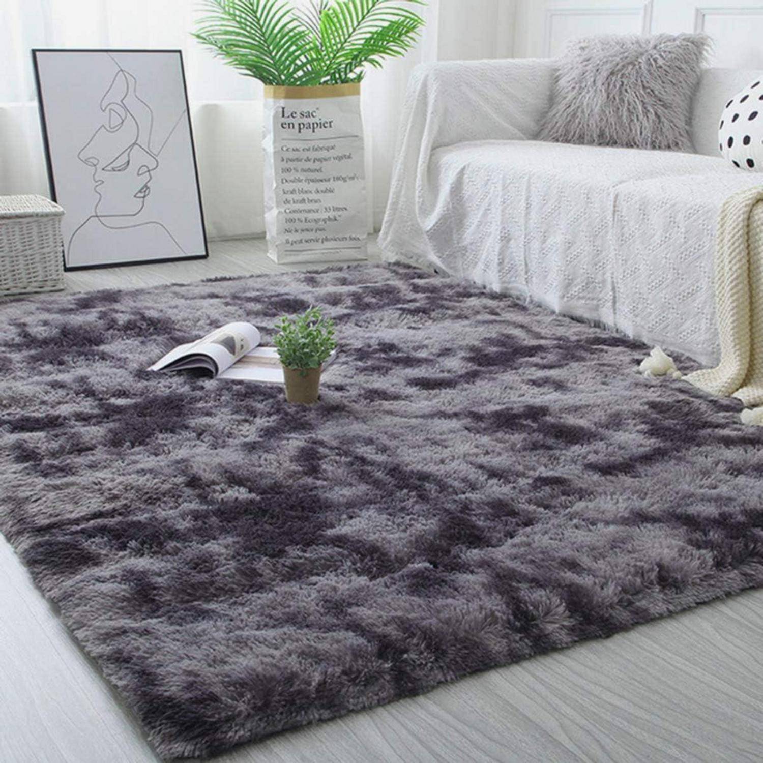 Ein grauer flauschiger Teppich in einem Wohnzimmer mit einem weißen Sofa, dekorativen Pflanzen und einer monochromen Wandkunst. Der Raum hat eine minimalistische Einrichtung.