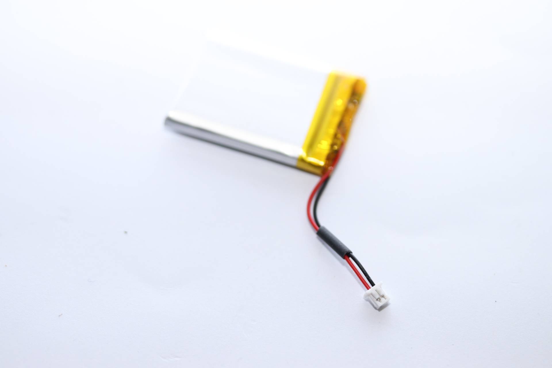 Eine kleine Lithium-Polymer-Batterie mit einem gelben Deckel und roten und schwarzen Kabeln, auf einem einfarbigen weißen Hintergrund.