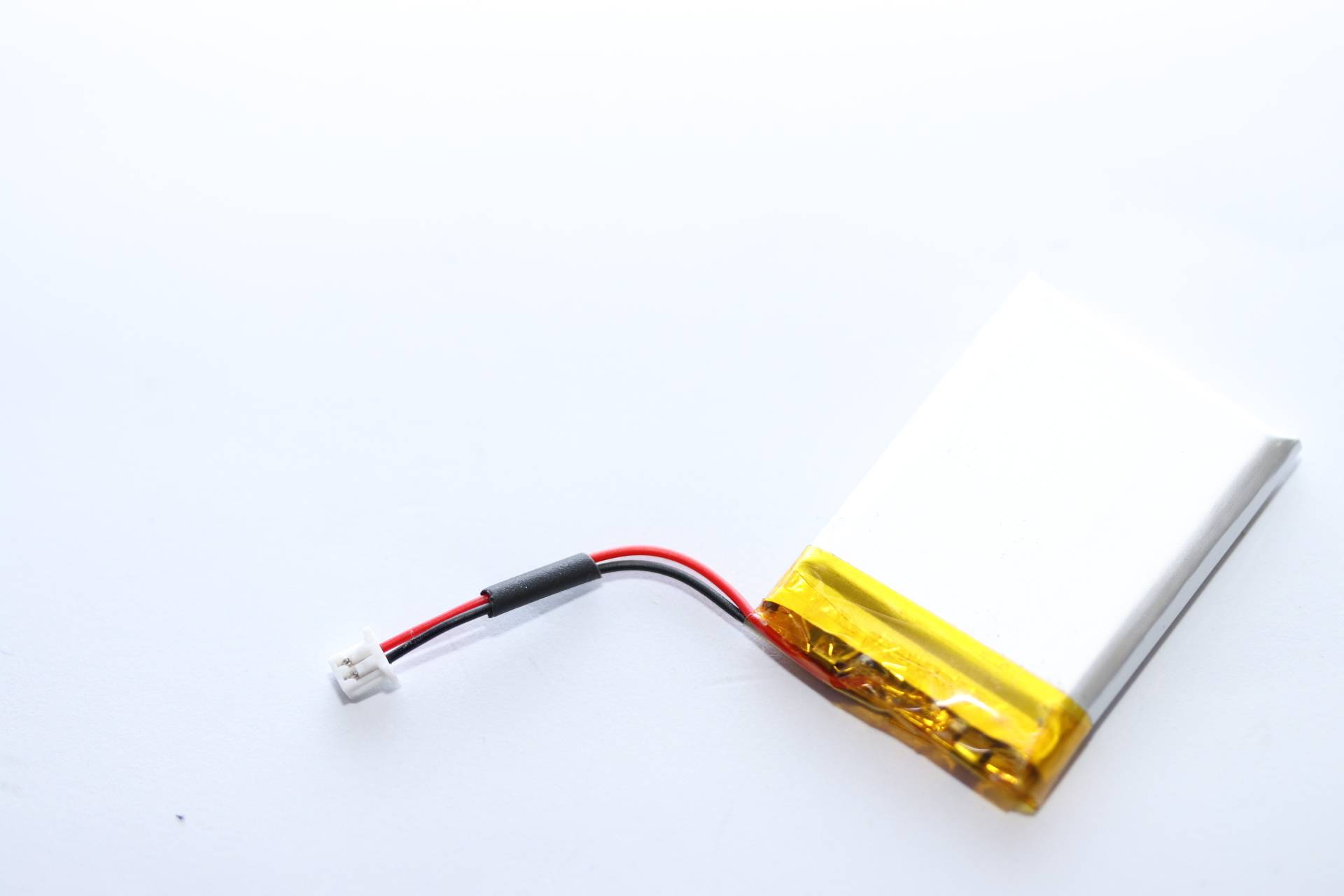 Eine kleine Lithium-Polymer-Batterie mit einem gelb-silbernen Gehäuse, verbunden mit schwarzen und roten Kabeln und einem weißen Stecker.