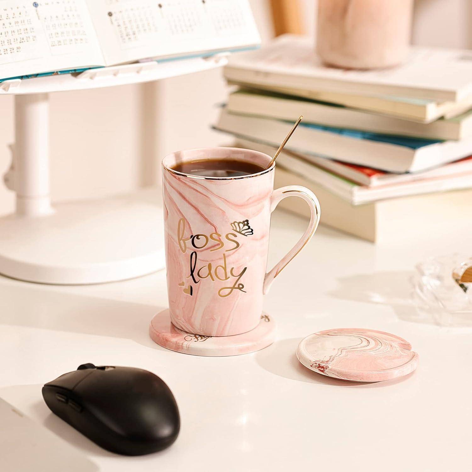 Eine Kaffeetasse mit der Aufschrift ‚Boss Lady' steht auf einem Schreibtisch neben einem Stapel Bücher, einer Computermaus und einem Papierkalender.