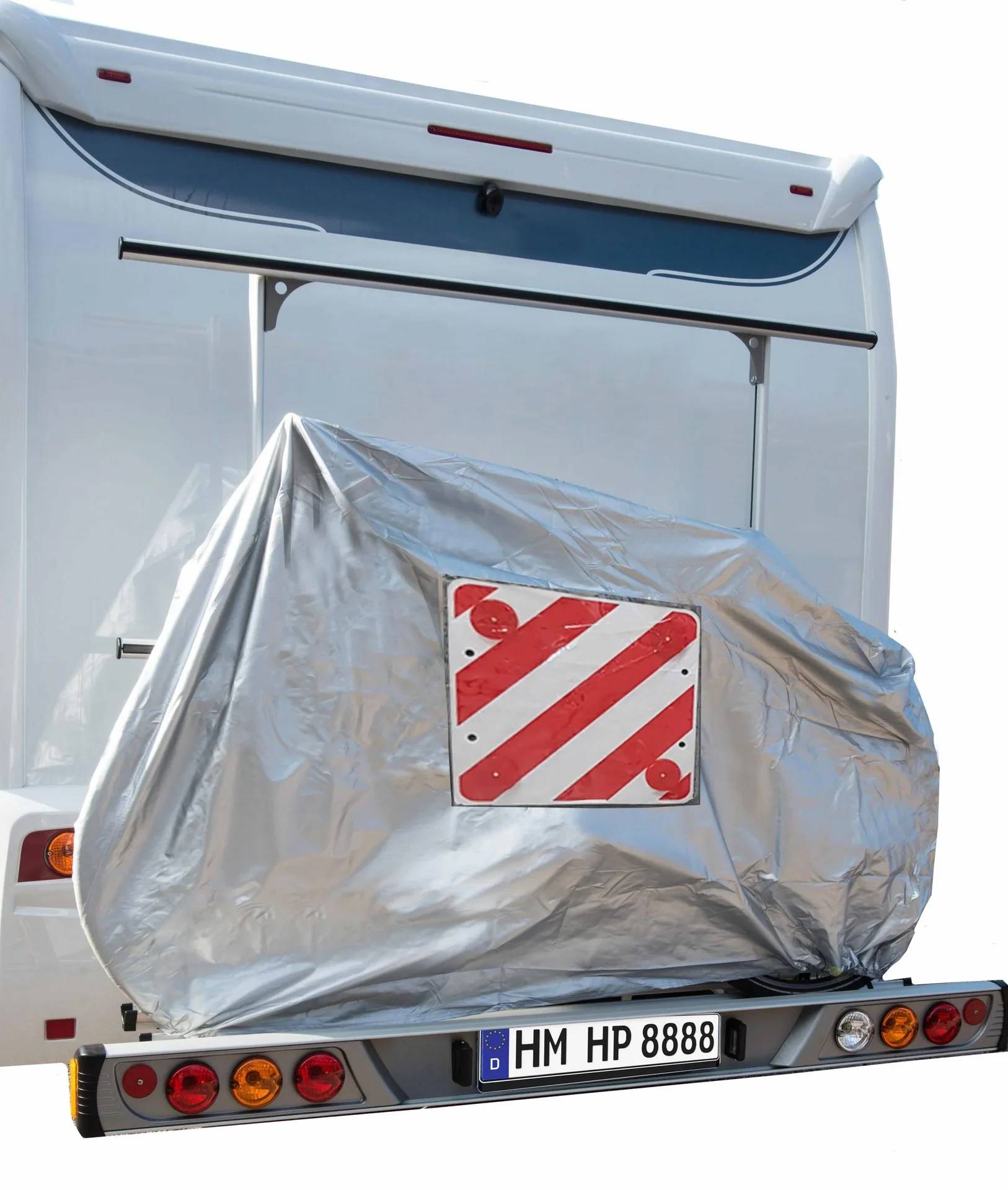 Rückseite eines Fahrzeugs mit einem großen, abgedeckten Objekt, das montiert ist und ein rot-weiß gestreiftes Warnschild zeigt.